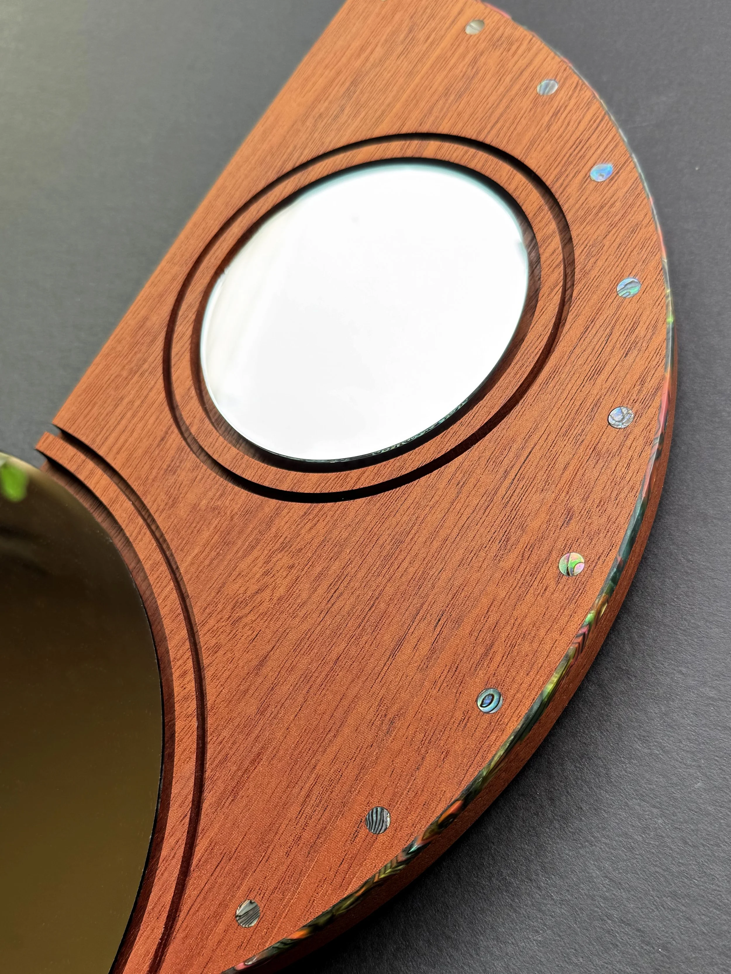 Mirrors with a colorful binding or purfling on the edges and abalone inlays on the front are an artisan technique used in in the detail of guitar necks.