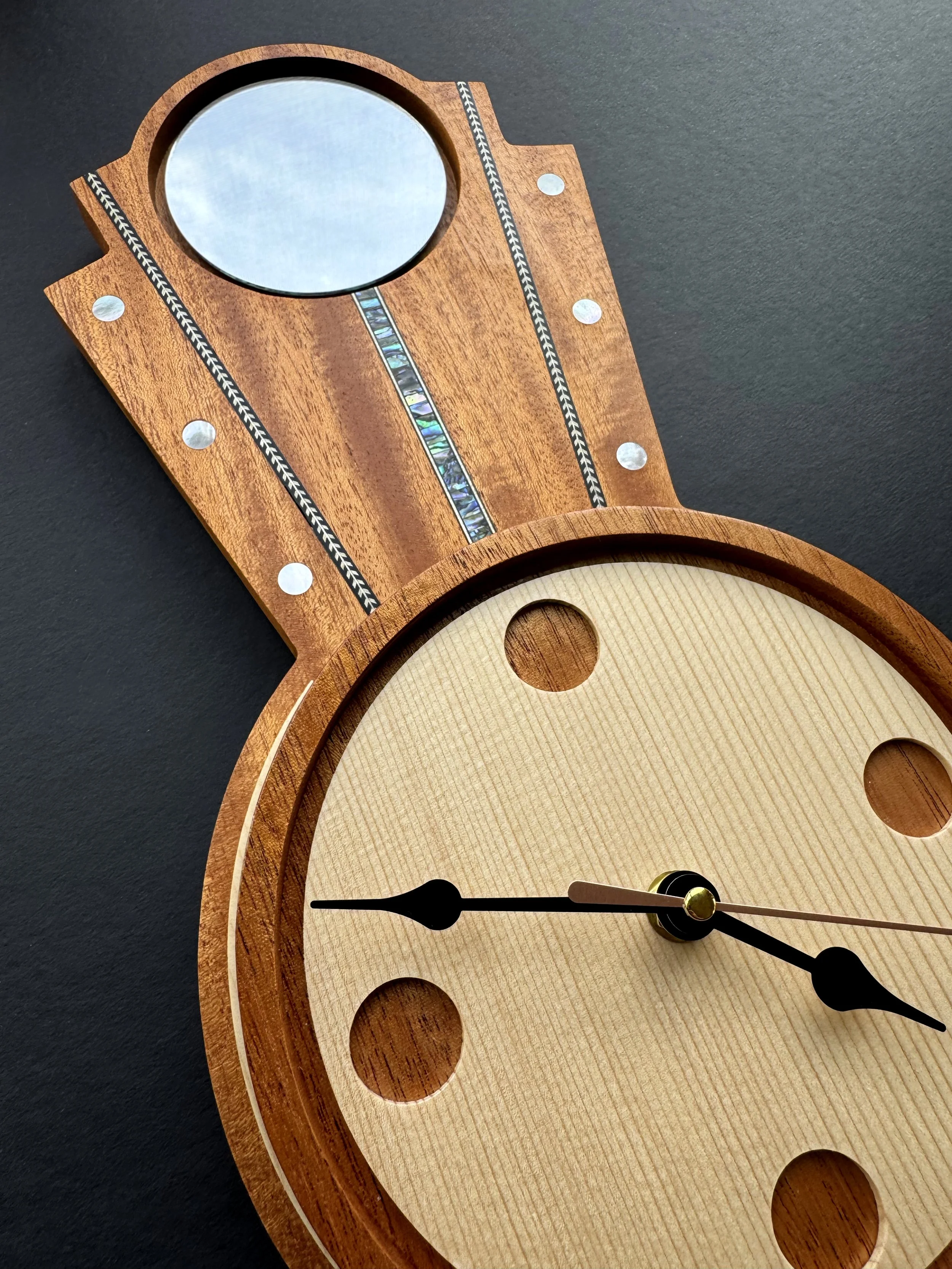 Close-up of a wooden clock with a light-colored face, black hour and minute hands, and a second hand, set on a black surface.
