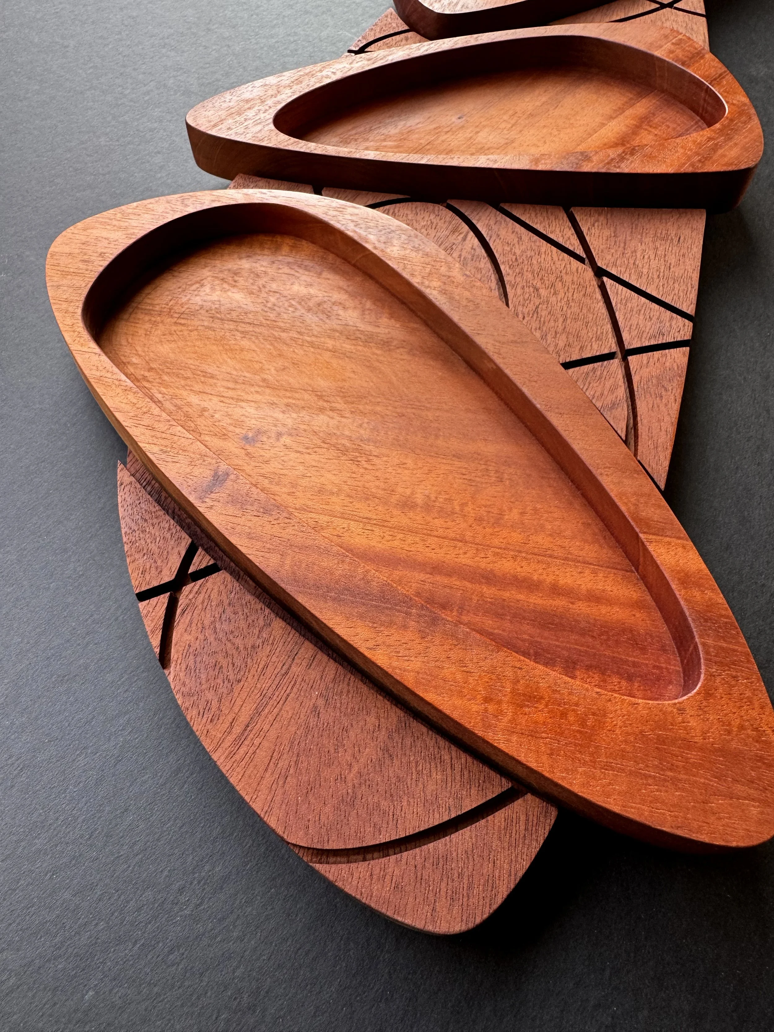 Two wooden trays with oval-shaped indentations on a dark surface.