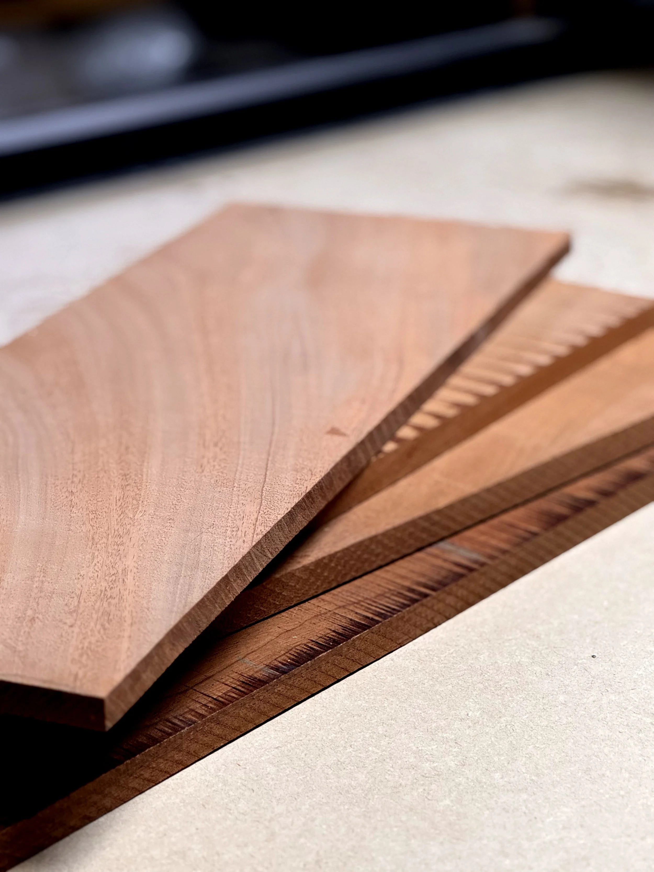 Close-up of a stack of cut wooden planks arranged in a fanned-out manner on a light surface.