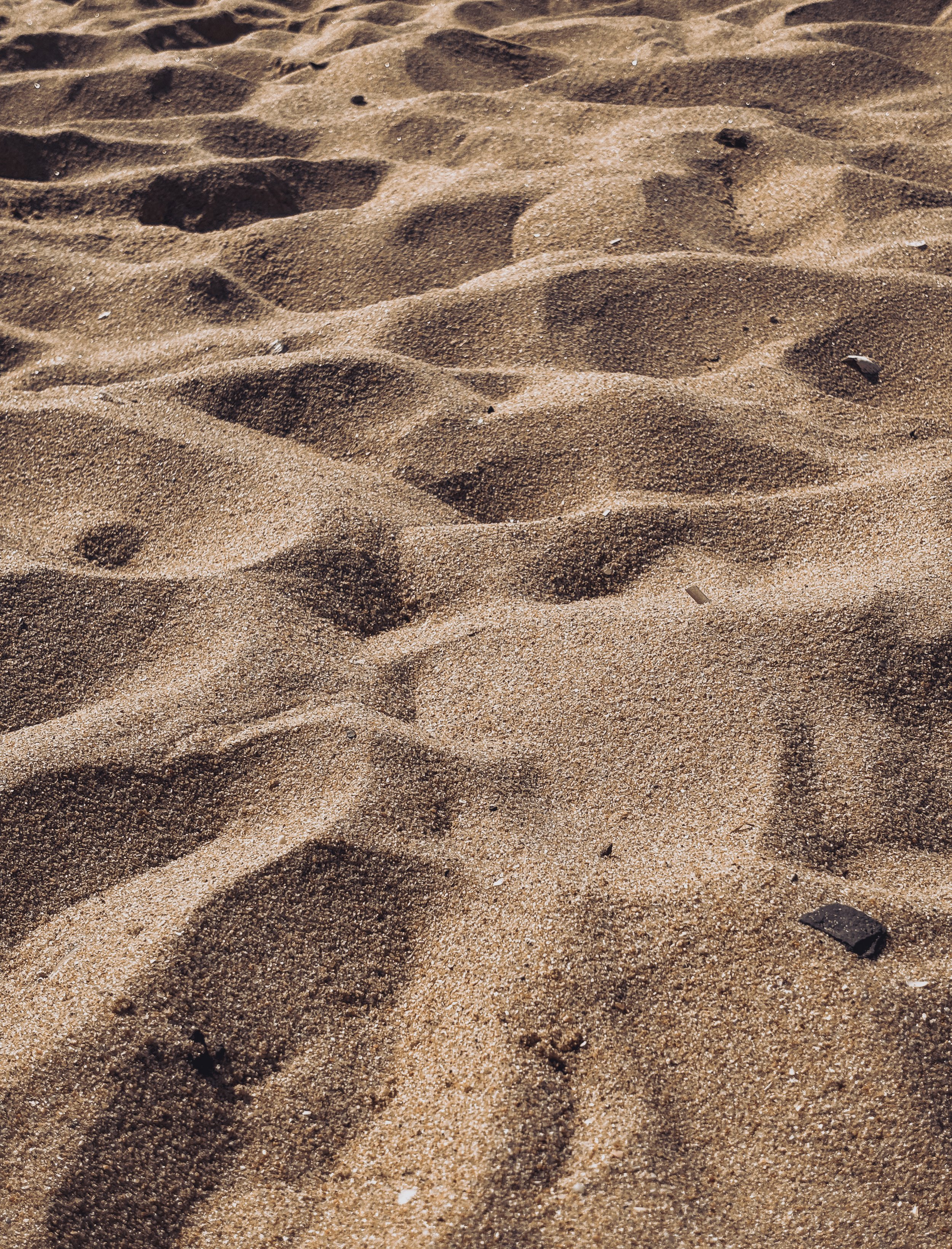 Close-up of sandy beach with footprints and small scattered rocks.