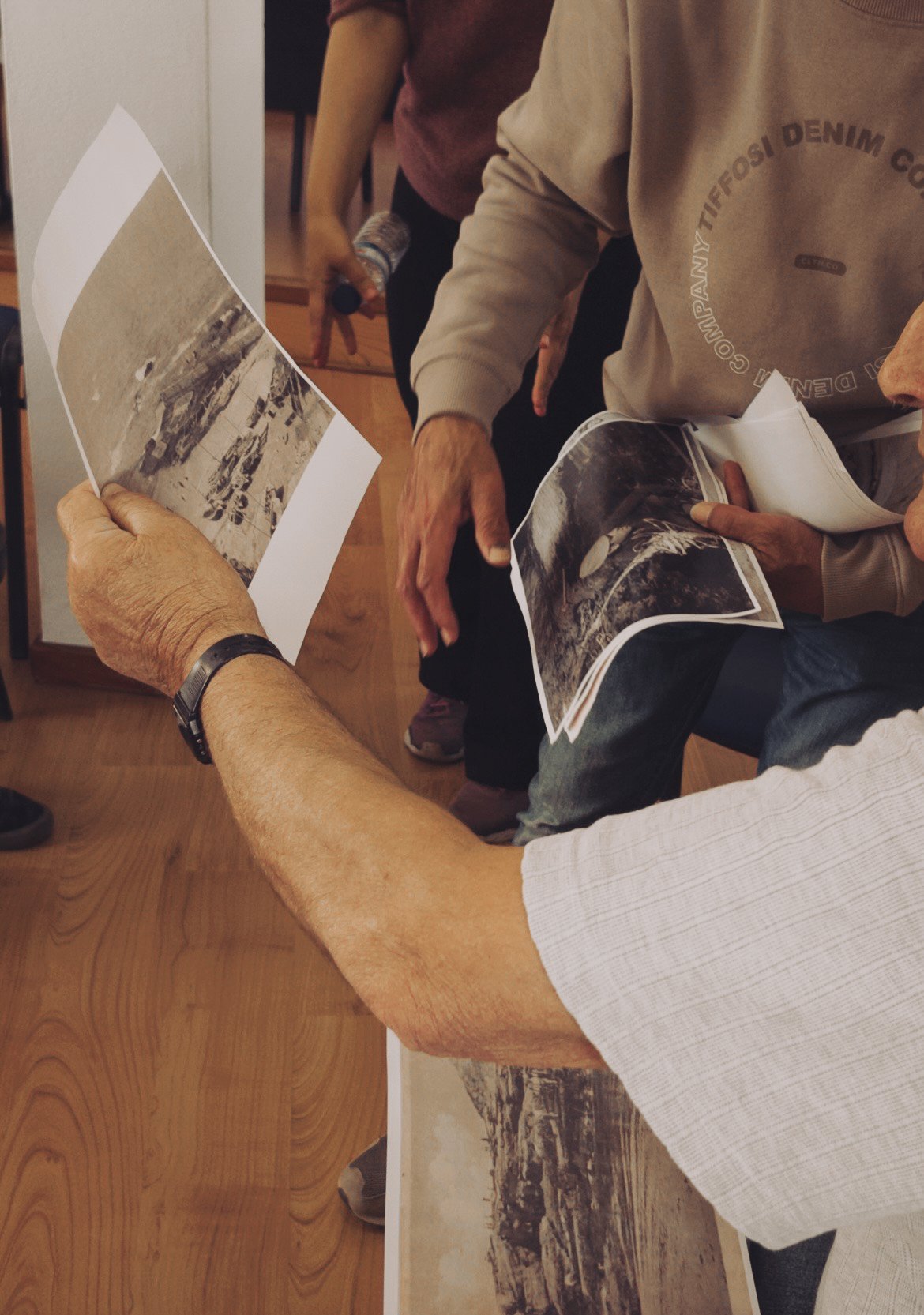 People examining black and white photographs of landscapes or scenes, holding printed photos, in an indoor setting.