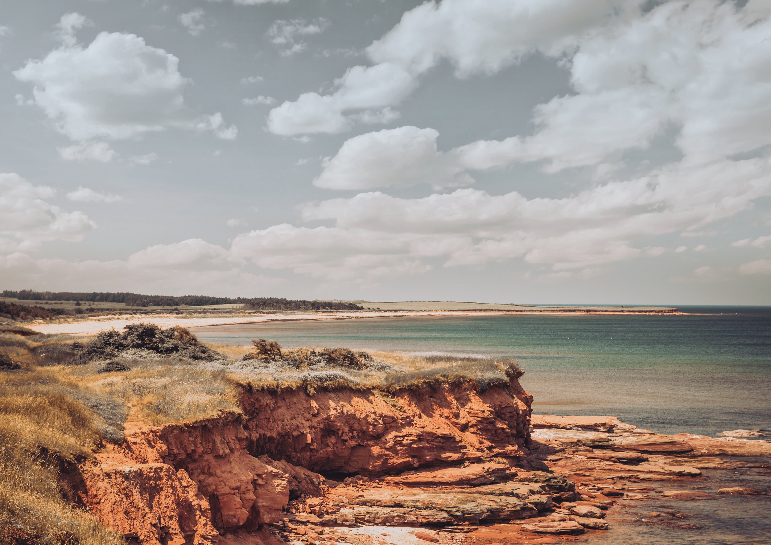 Cliffs overlooking a body of water with a sandy beach and cloudy sky.