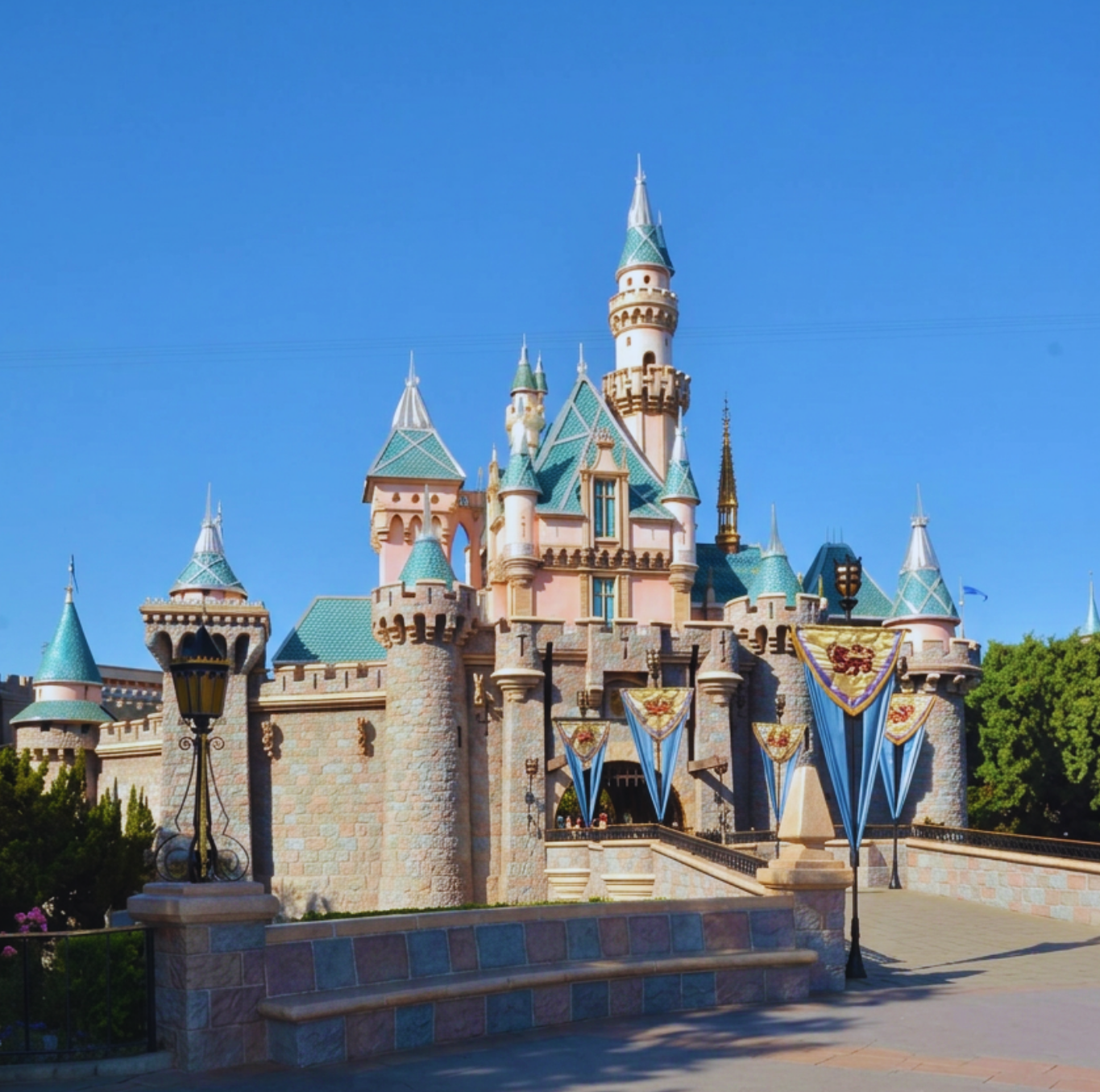 Disneyland castle with pink walls, blue rooftops, and decorative banners under a clear blue sky.