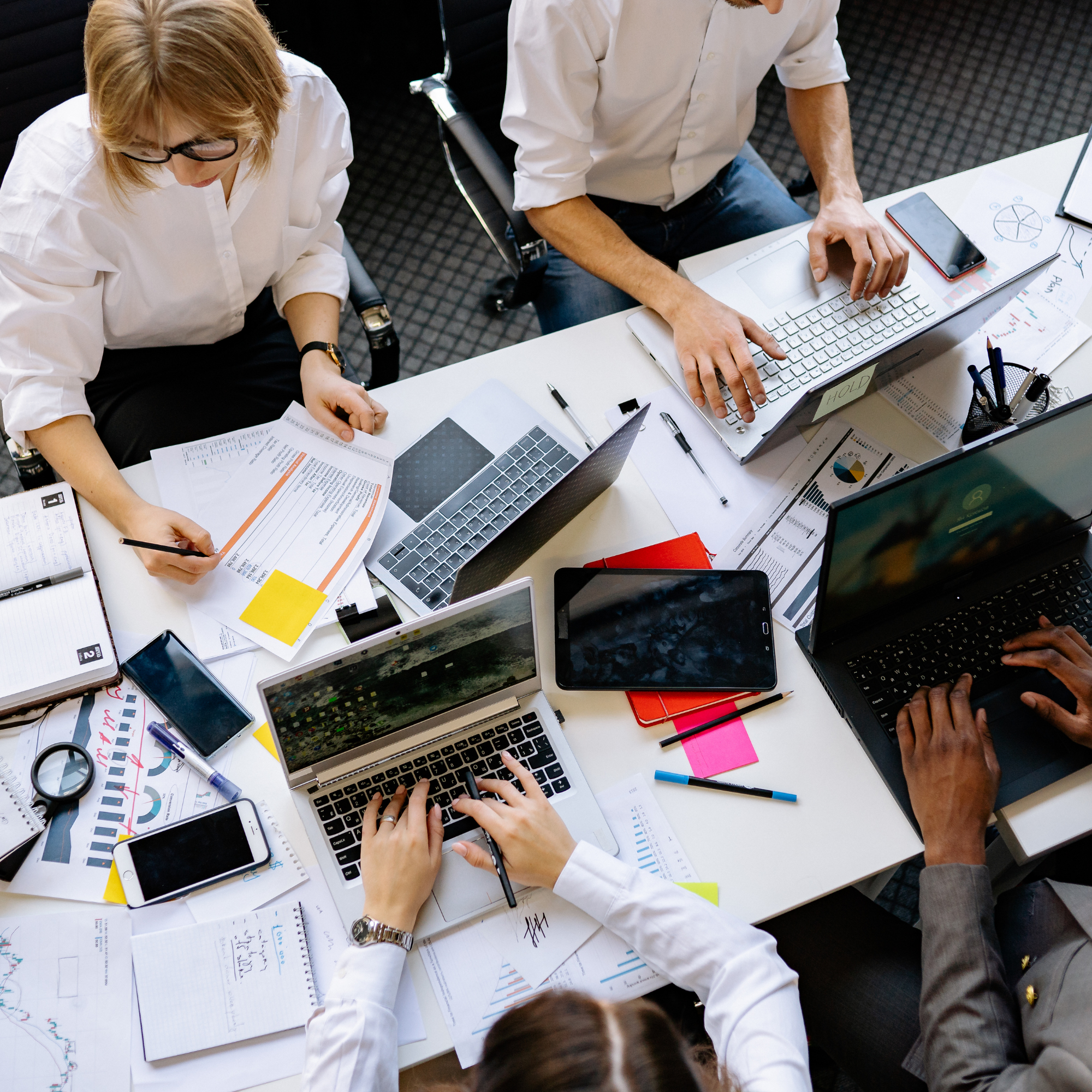 People working at a desk with laptops, documents, and smartphones, collaborating on a project.