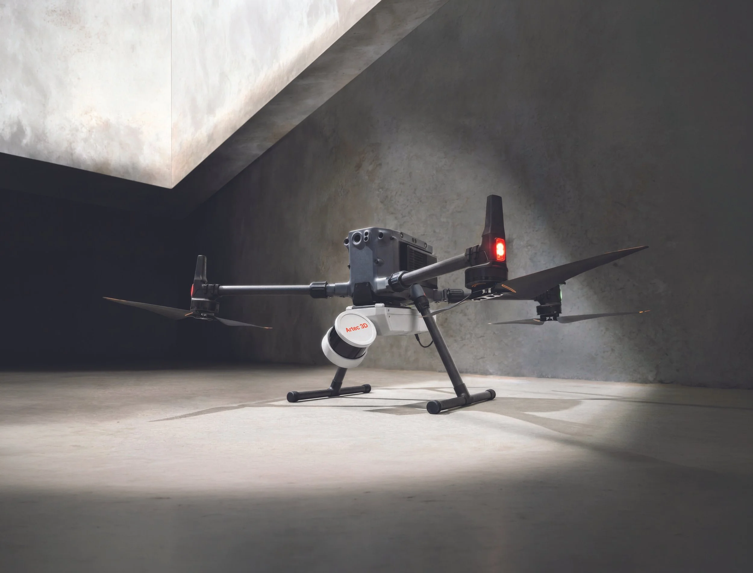 A drone with a camera mounted on it, resting on a concrete floor in an industrial-style room with concrete walls and a ceiling.