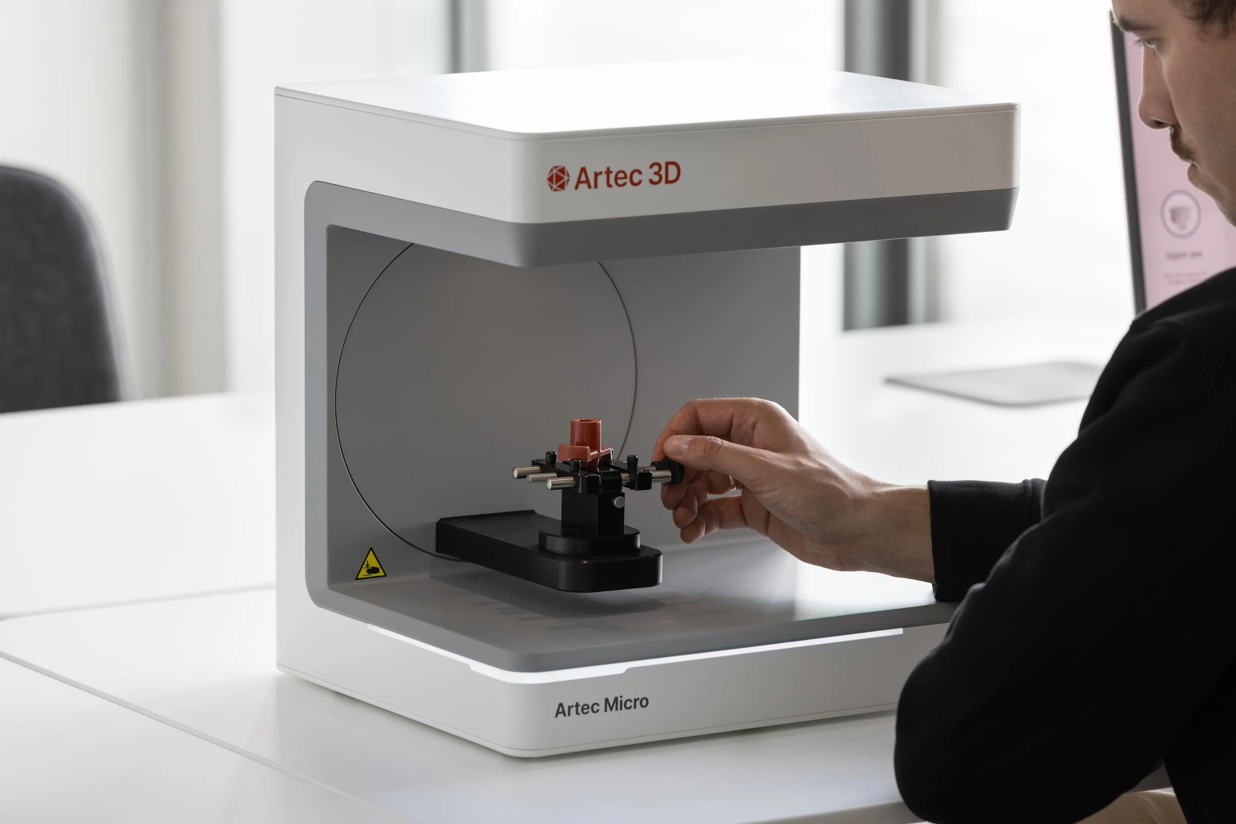 A person operating an Artec Micro 3D scanner on a white table in a modern office setting.