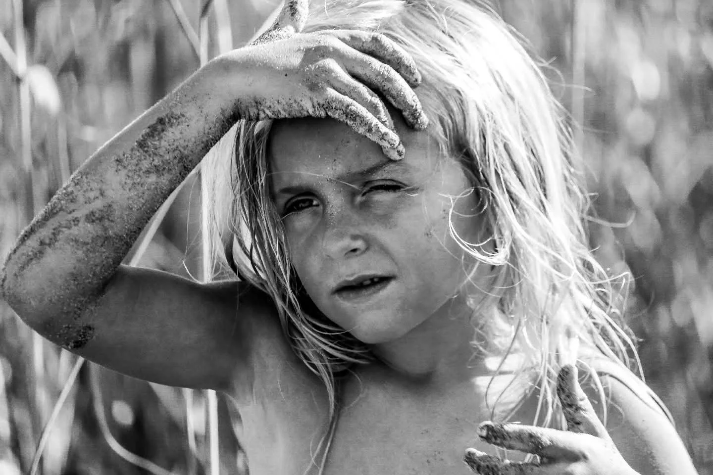 Black and white photo of a young girl with wet, messy hair, covered in dirt. She is shielding her eyes from the sun with one hand, and the other hand is touching her chest.