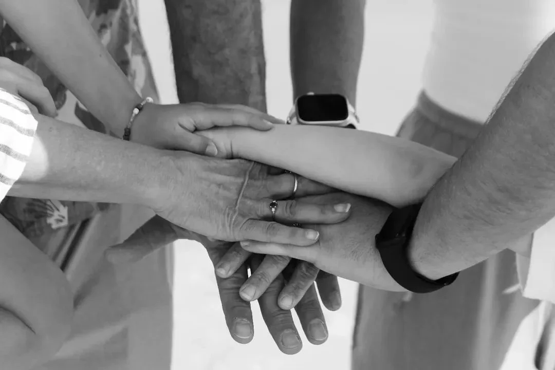 Multiple hands stacked together, showing unity or teamwork, with a smartwatch on one wrist and rings on others.