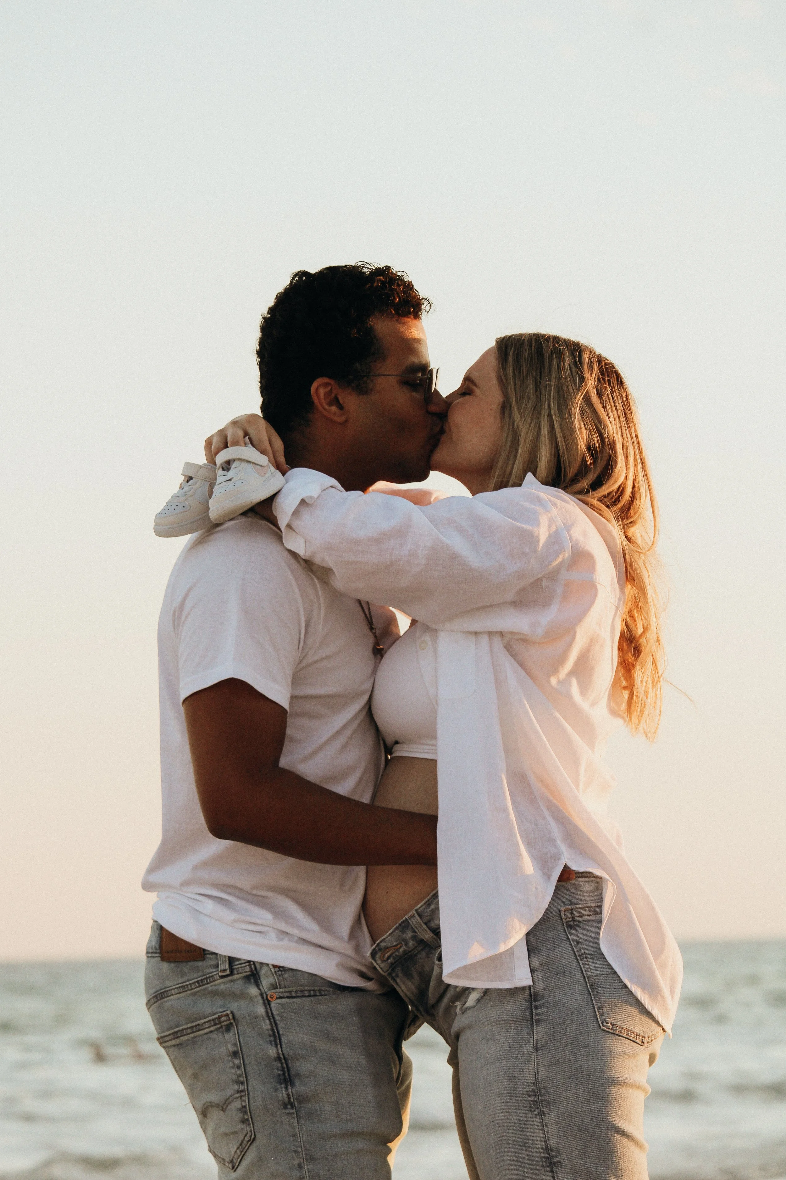 A couple kissing on a beach at sunset, with the woman holding a child in her arms.