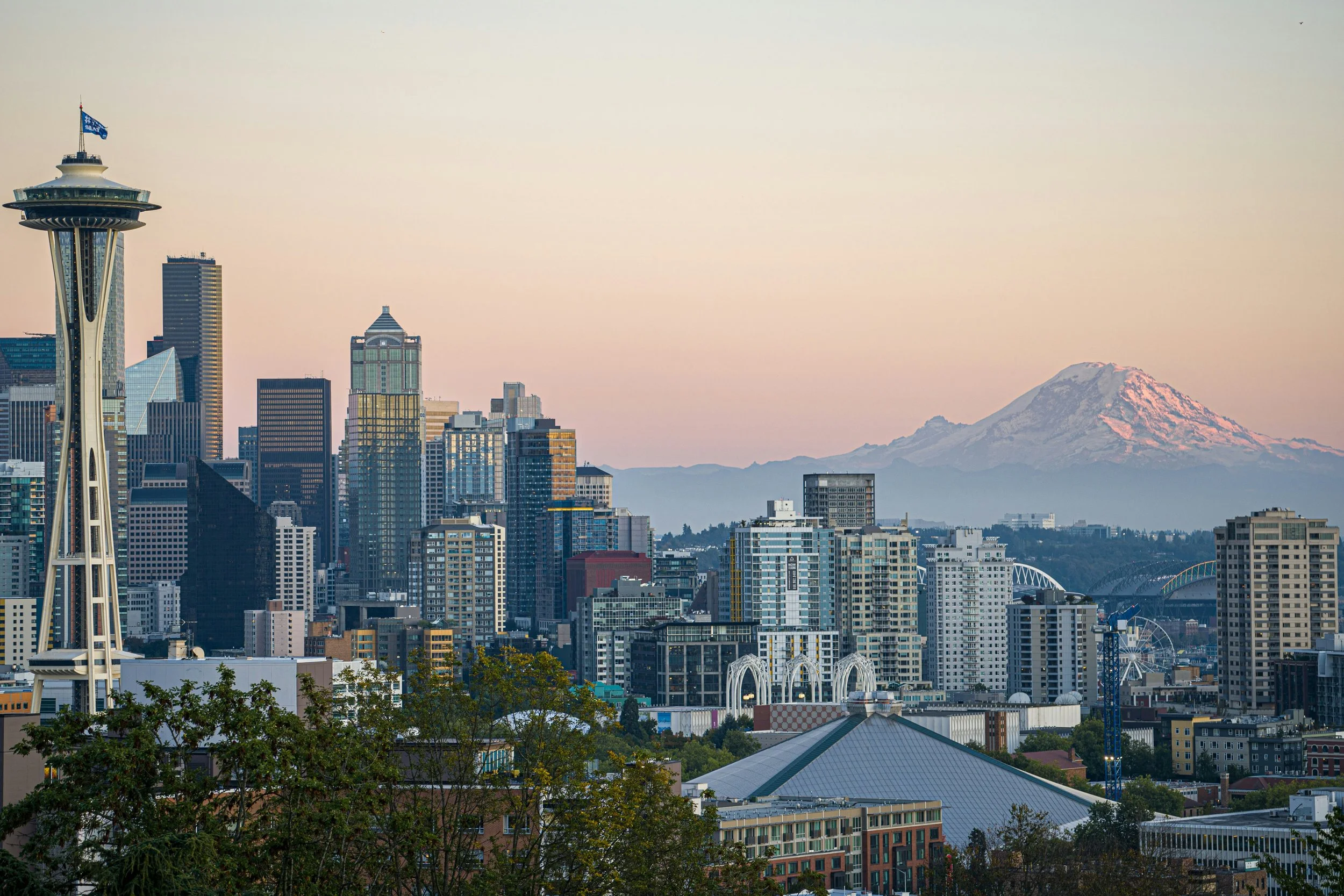 Skyline of Seattle city with the Space Needle in the foreground and Mount Rainier in the background at sunset.