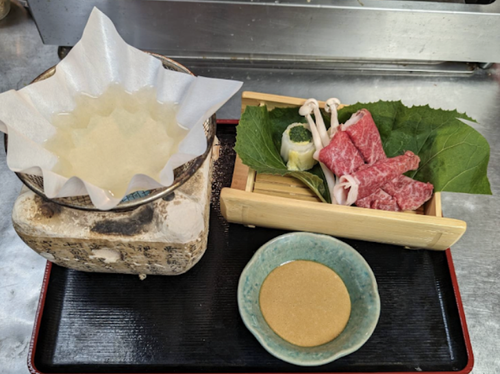 Arrangement of ingredients for Japanese hot pot, including sliced raw beef, vegetables, and dipping sauce on a black tray.
