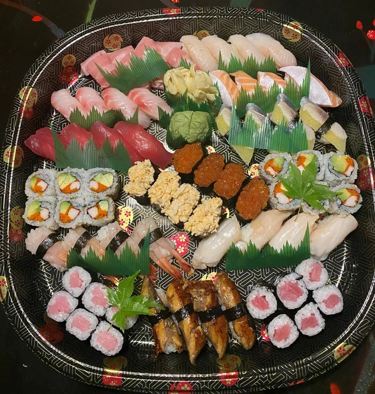 A large platter of assorted sushi, including nigiri, sashimi, and various sushi rolls with different fish, shrimp, and roe toppings on a black decorative tray.