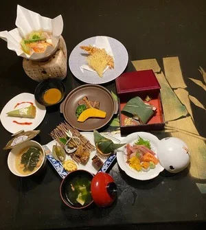A traditional Japanese meal with various dishes including sashimi, tempura, soup, and condiments, displayed on multiple small plates and bowls.