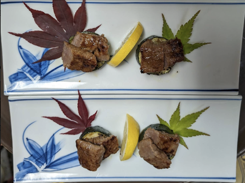 Two plates each with a piece of sushi topped with beef, a lemon wedge, and a decorative green or red maple leaf.