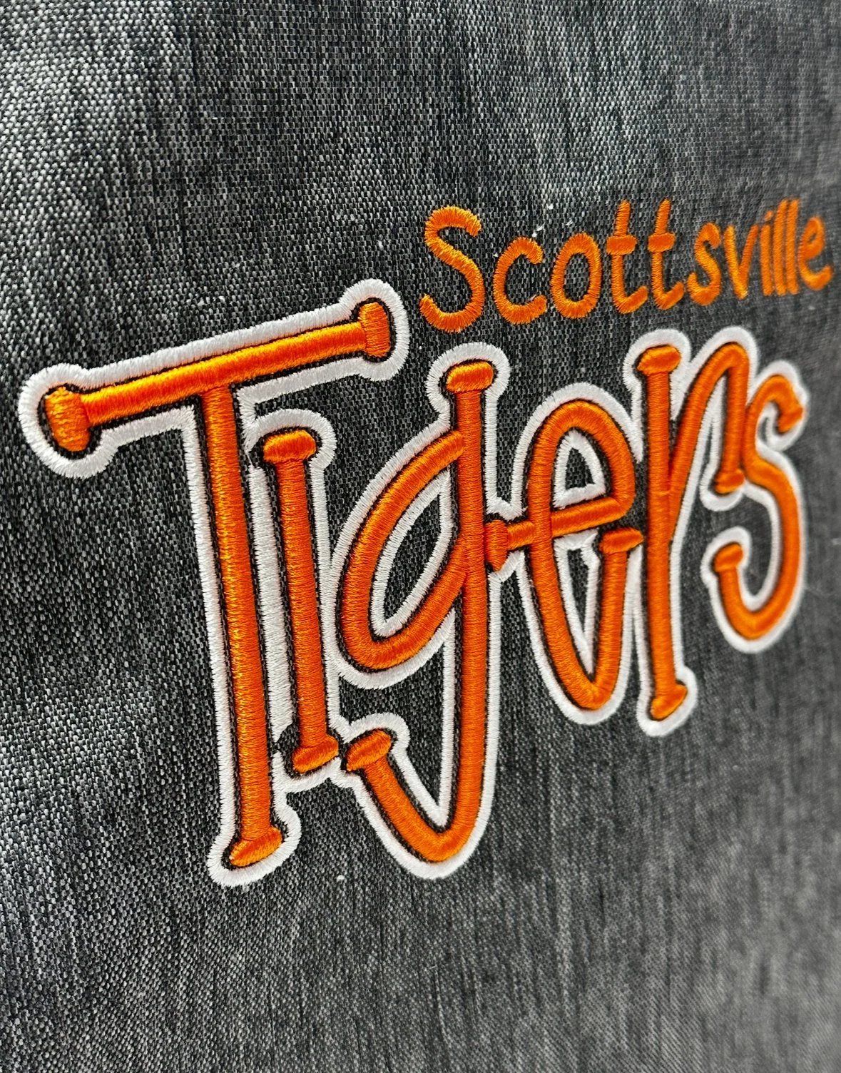 Close-up of an embroidered patch with the words "Scottsville Tigers" on dark fabric, with "Tigers" written in large orange cursive letters outlined in white.