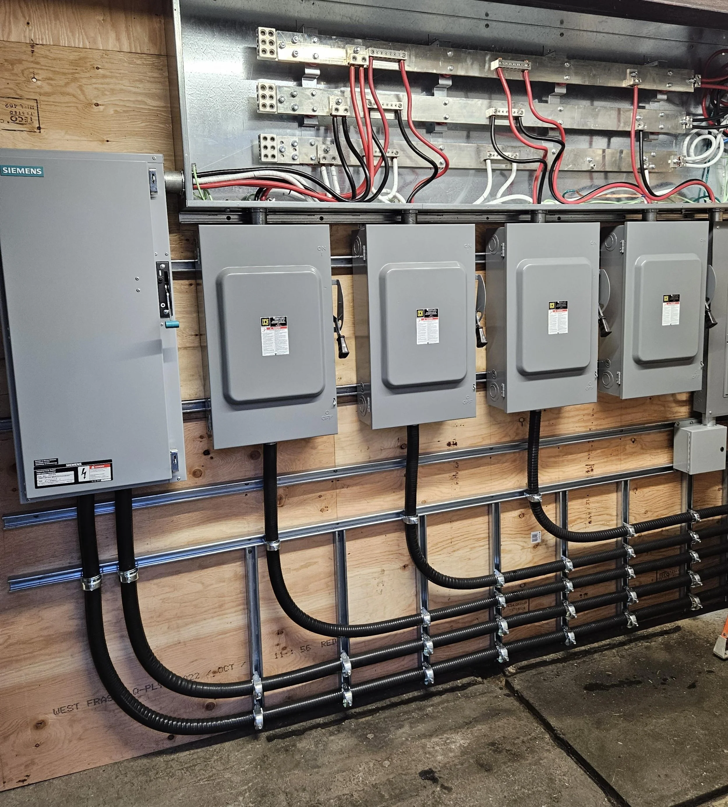 Electrical wiring and panels mounted on a wooden wall in an industrial or construction setting.