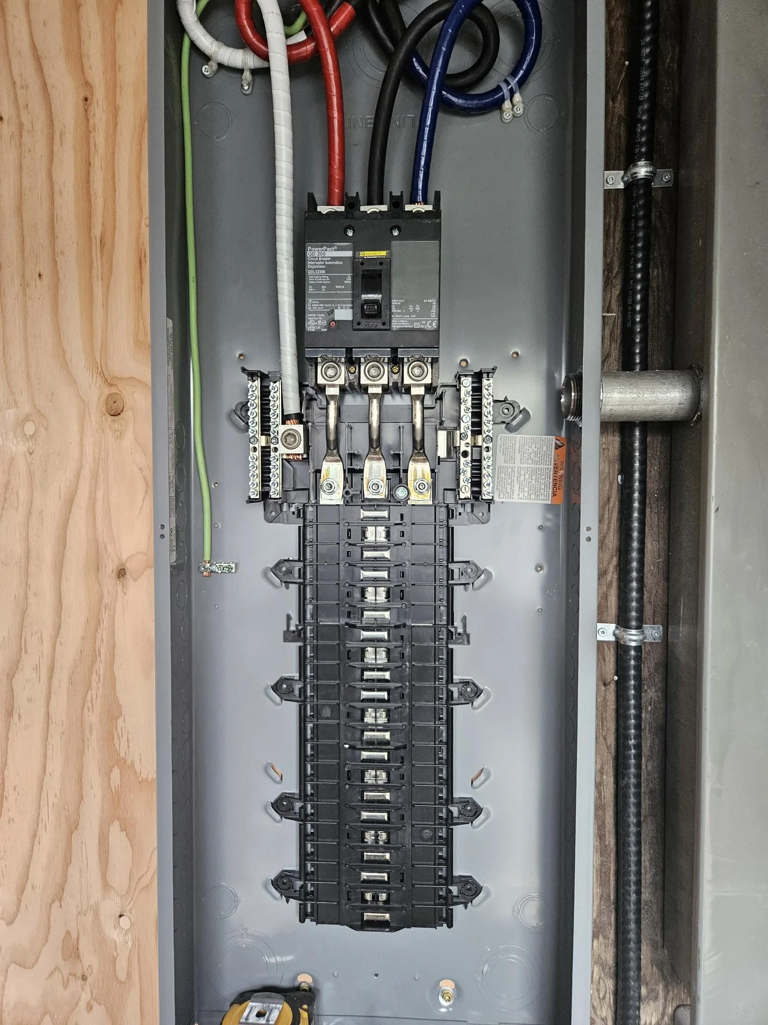 Interior view of an electrical panel with a circuit breaker, colored wires, and wiring connections on a metal backplane.