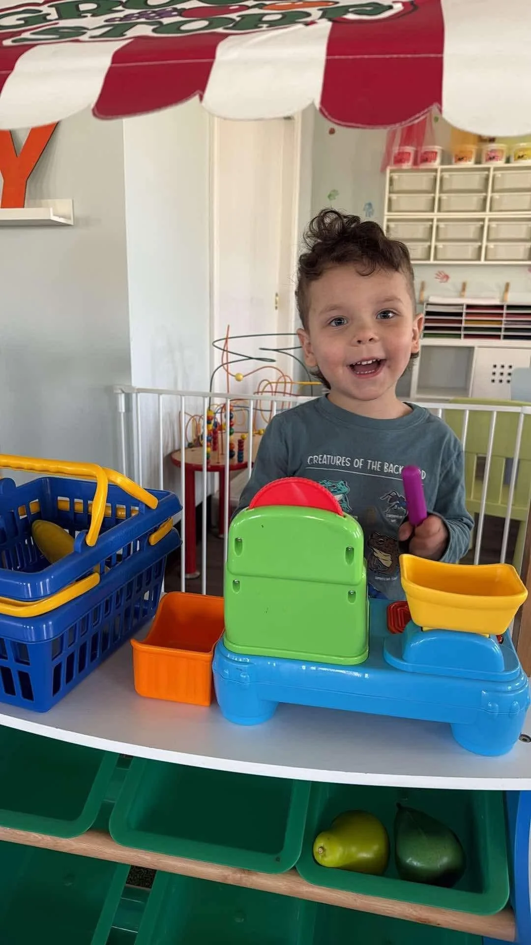 Young boy playing with colorful plastic toys at a play table in a child's playroom.