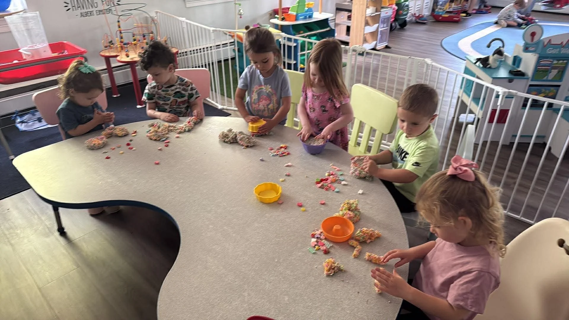 Children sitting at a table playing with colorful textured toys in a playroom.