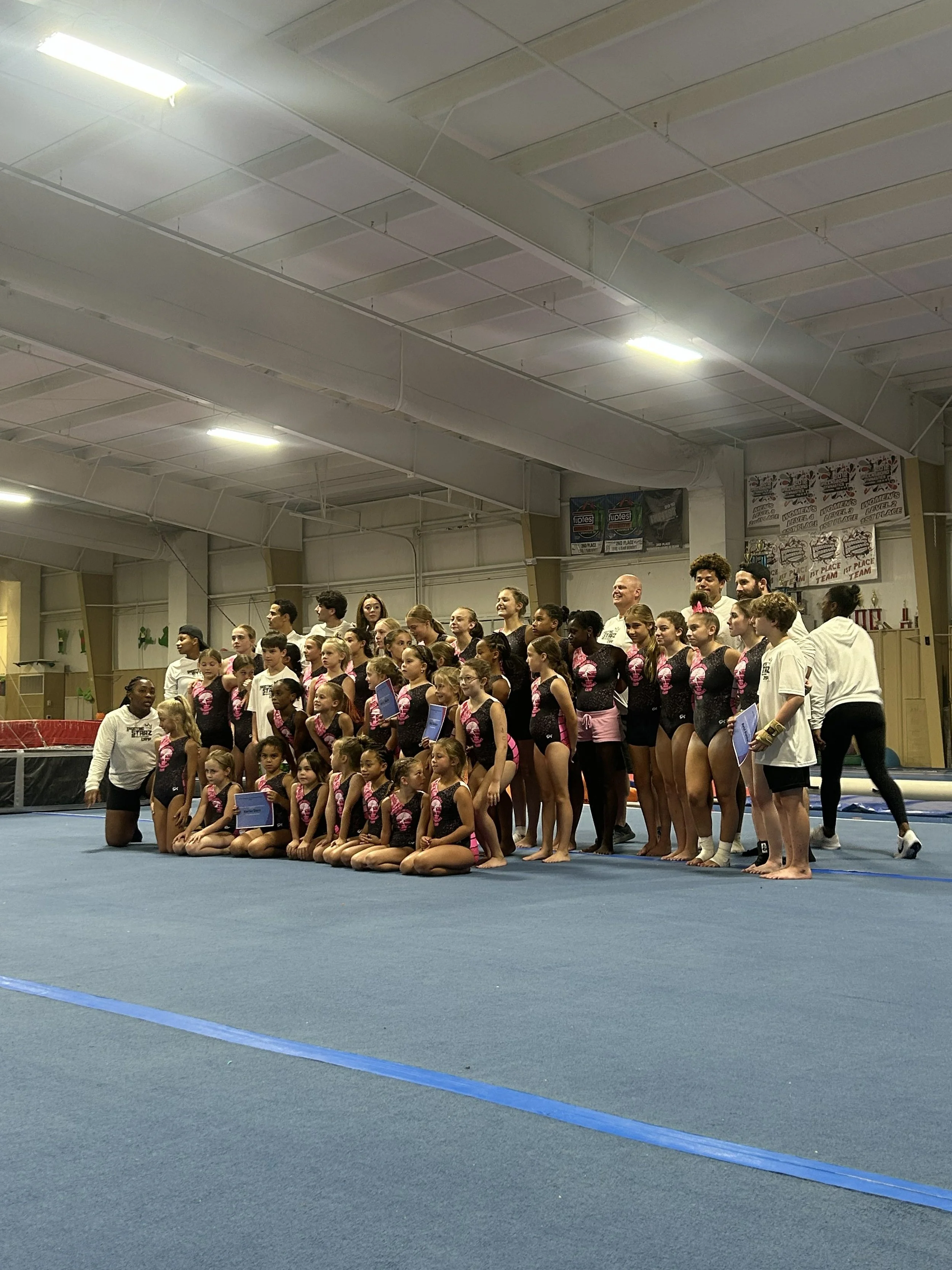 Group of young gymnasts and coaches posing together in an indoor gymnasium.