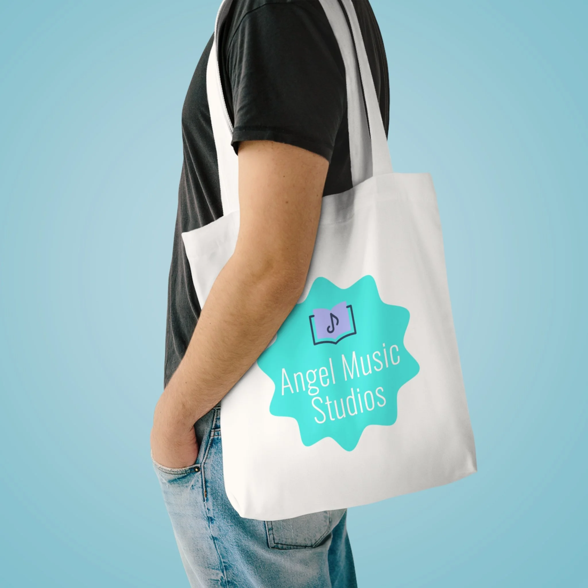 A person wearing a black t-shirt and blue jeans holding a white tote bag with a turquoise logo, standing against a light blue background.