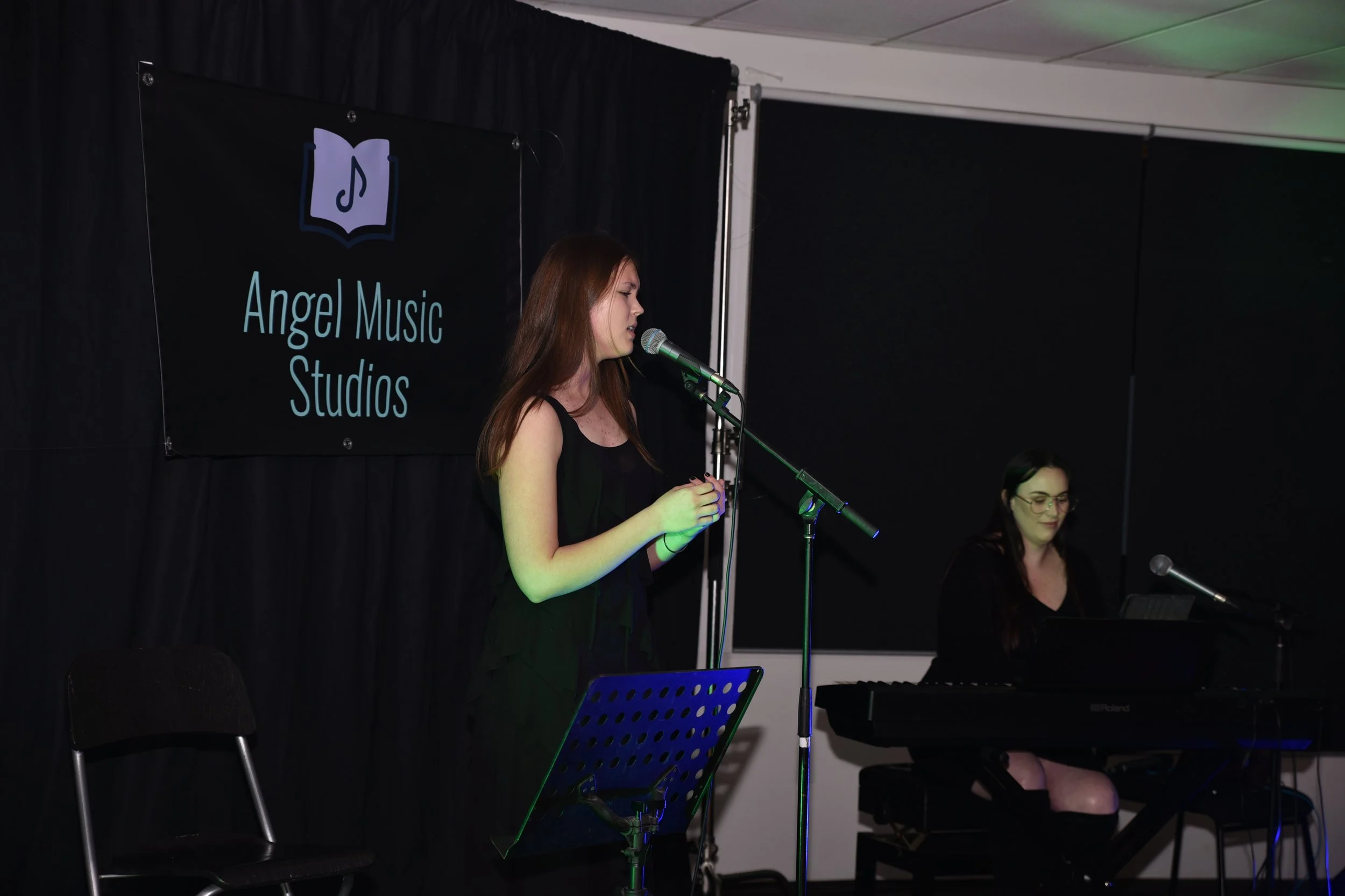 A woman singing on stage at Angel Music Studios with another woman playing keyboard beside her.