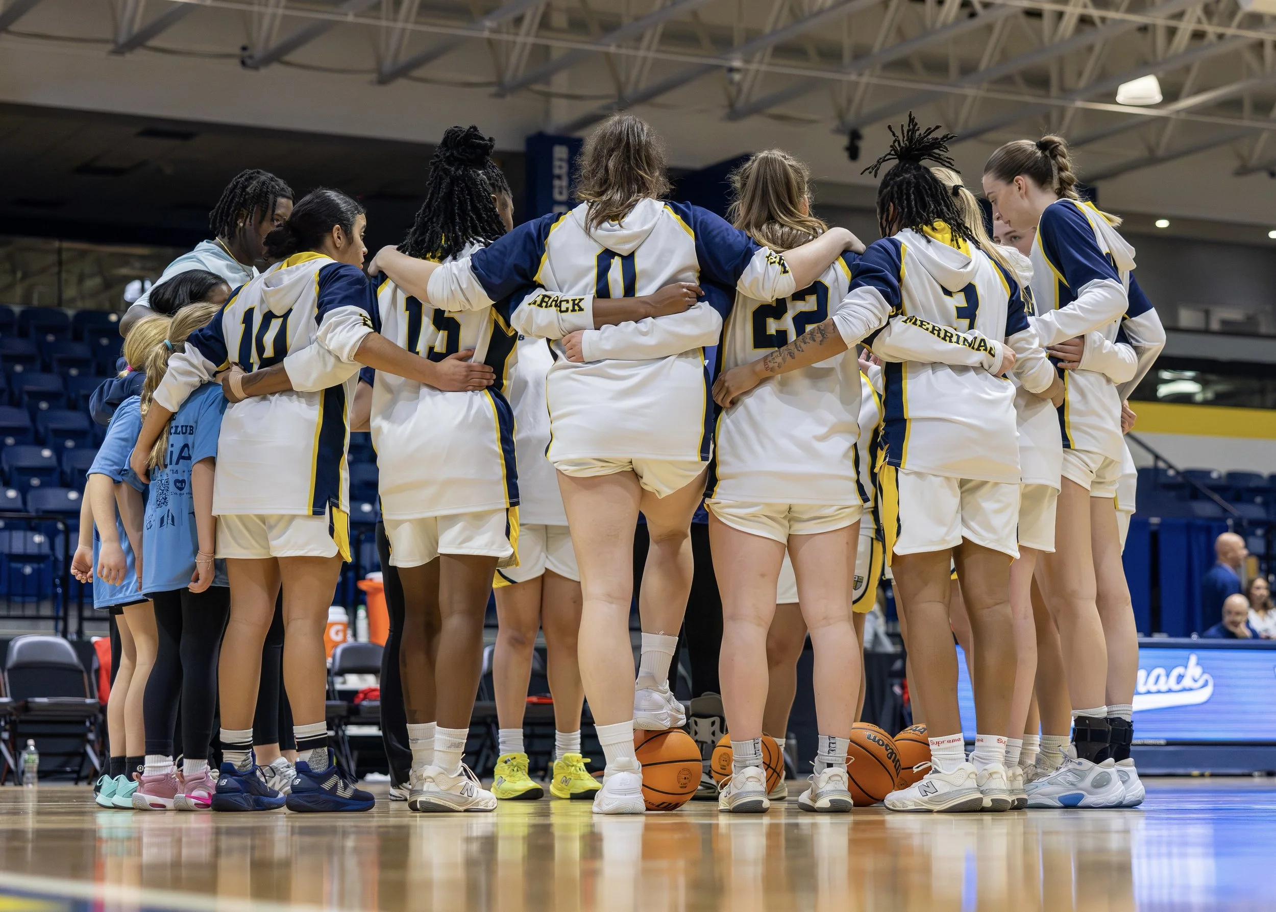 Women basketball players in a huddle during a game on an indoor court.