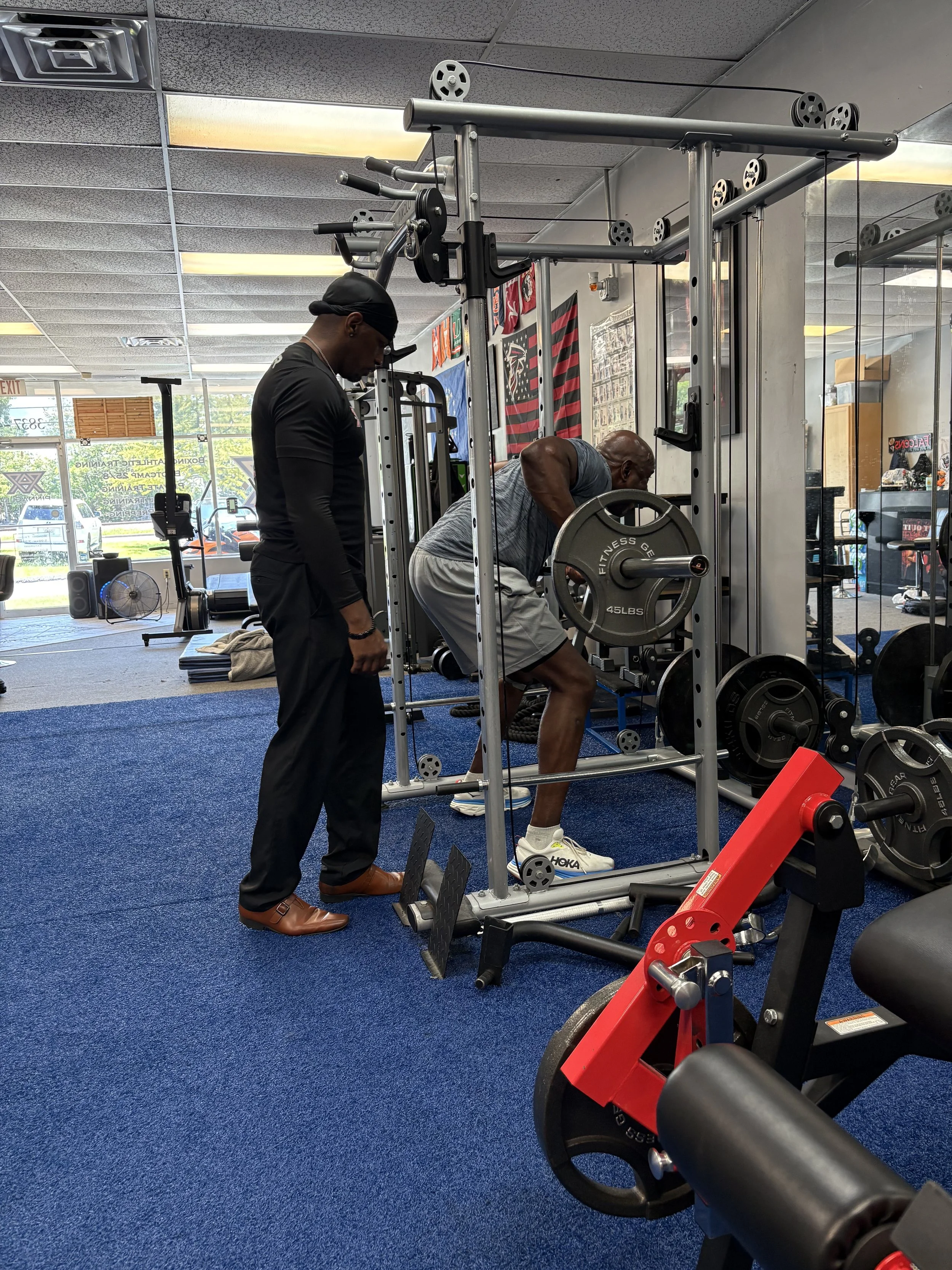 A man lifting weights with a trainer observing in a gym.