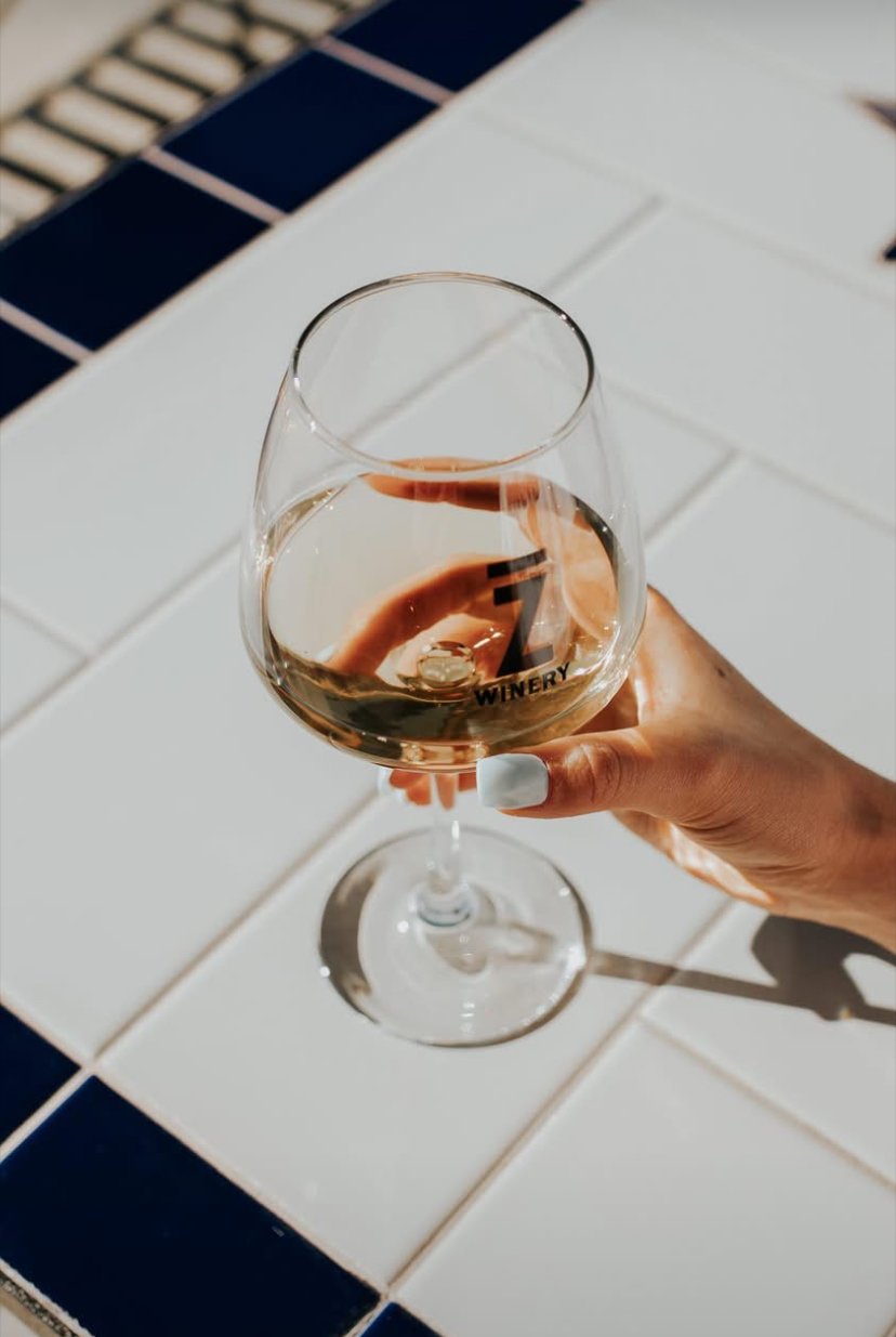 A glass of white wine held in a person's hand, with a white tiled surface and a blue tiled border in the background.