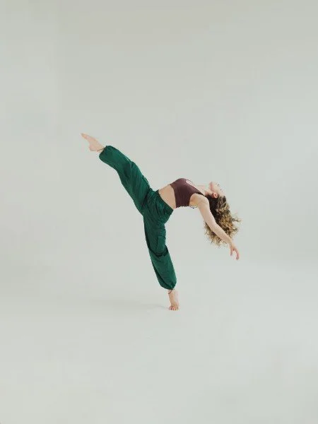A woman practicing a one-handed yoga pose on a plain light-colored background.