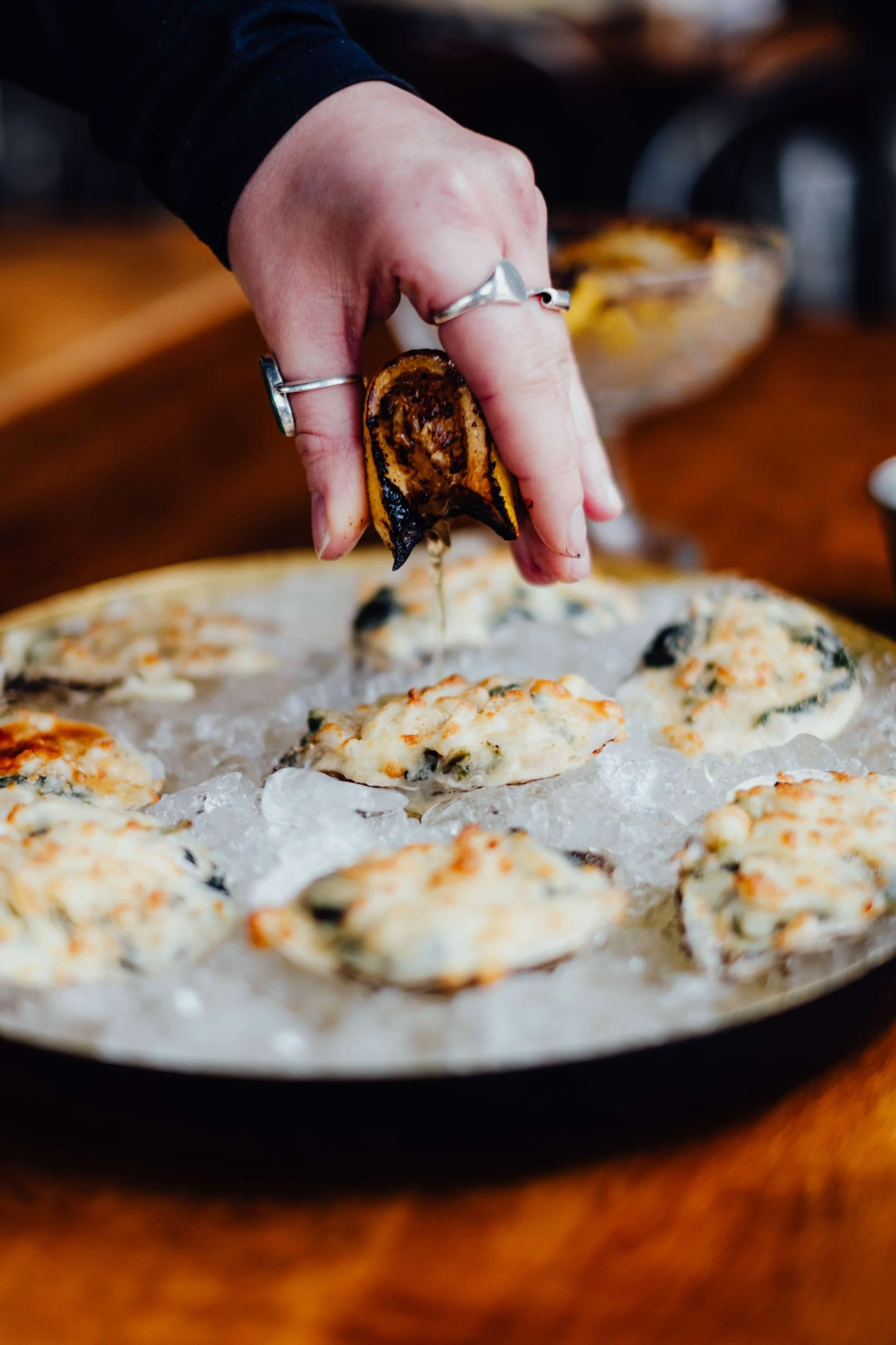 Une main tenant une tranche d'aubergine grillée, au-dessus de petits pains ou quiches avec des légumes, sur une plaque chauffante.