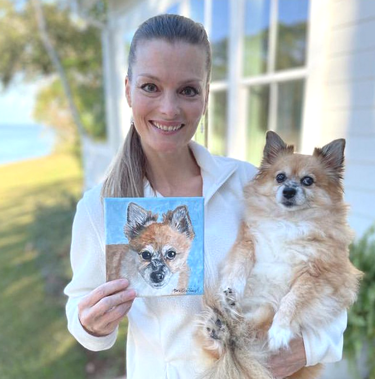Photo of a smiling woman holding her dog and a painting of the dog