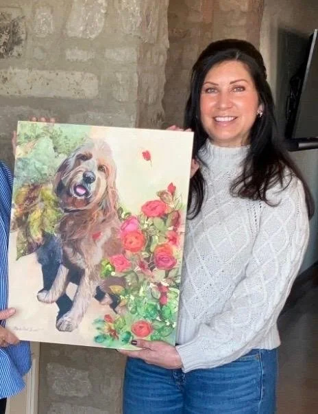 Photo of a smiling woman holding a painting of her dog