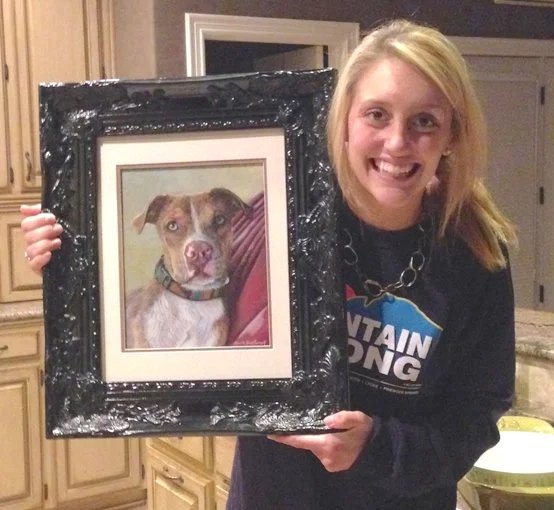 Photo of a smiling woman holding a painting of her dog