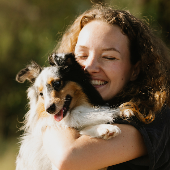 Photo of a woman, eyes closed, hugging a young Sheltie to her face.
