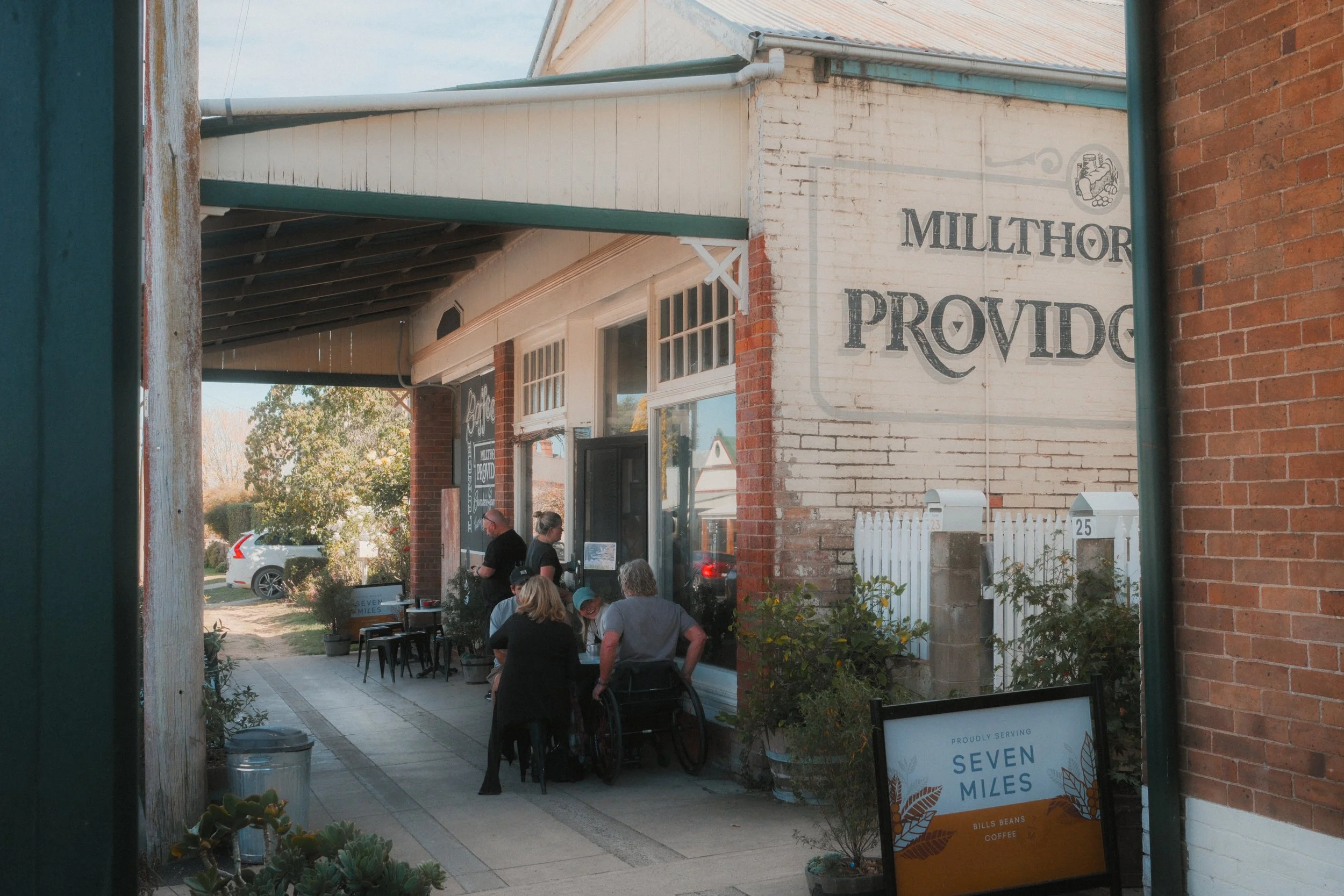 People seated outside a historic brick building in Millthorpe, with a painted Providence sign, café tables and warm village street scenery.