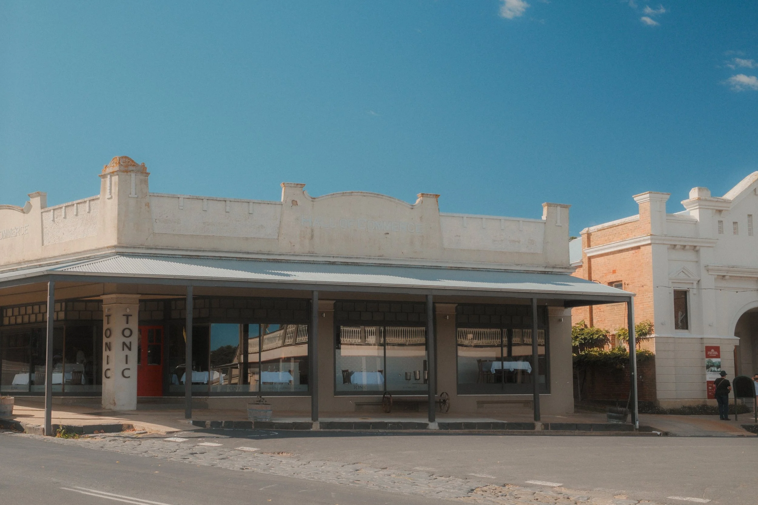 Historic cream storefront in Millthorpe with a wraparound verandah, large windows and Tonic signage under a clear blue sky.