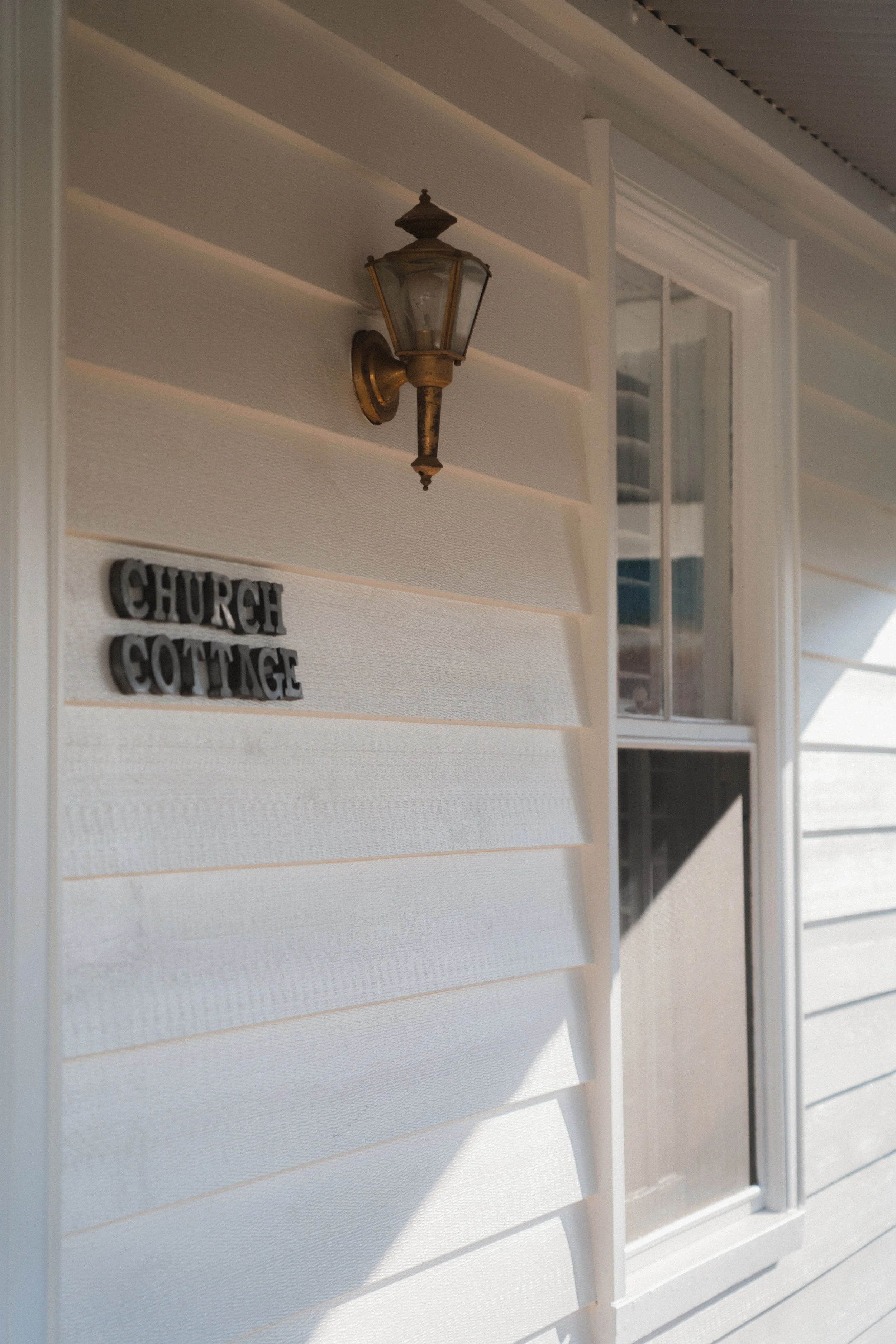 Close-up of a section of a house's exterior wall with a brass outdoor wall light and a sign reading 'Church Cottage'.