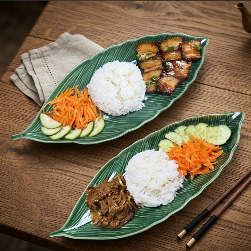 Deux plats de restauration asiatique avec riz blanc, légumes, viande grillée ou sautée, servis sur des assiettes en forme de feuille. Chopsticks à côté.