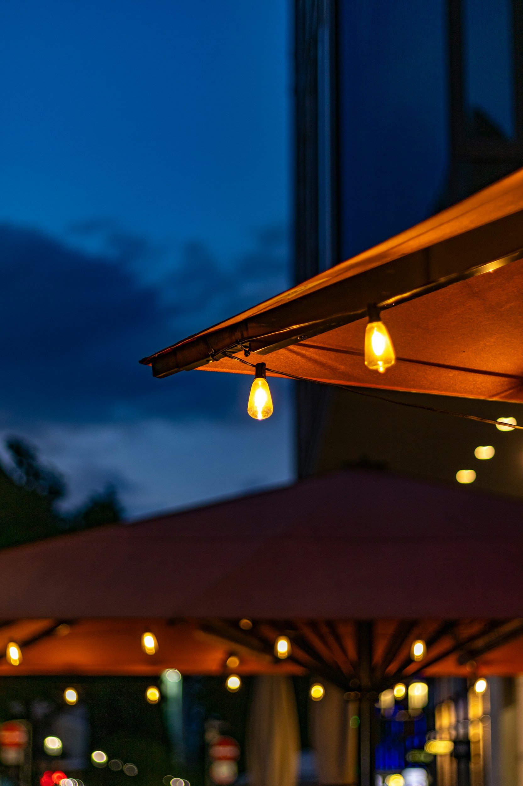 Night scene of a street with string lights hanging under an awning, blurred background with bokeh of lights.