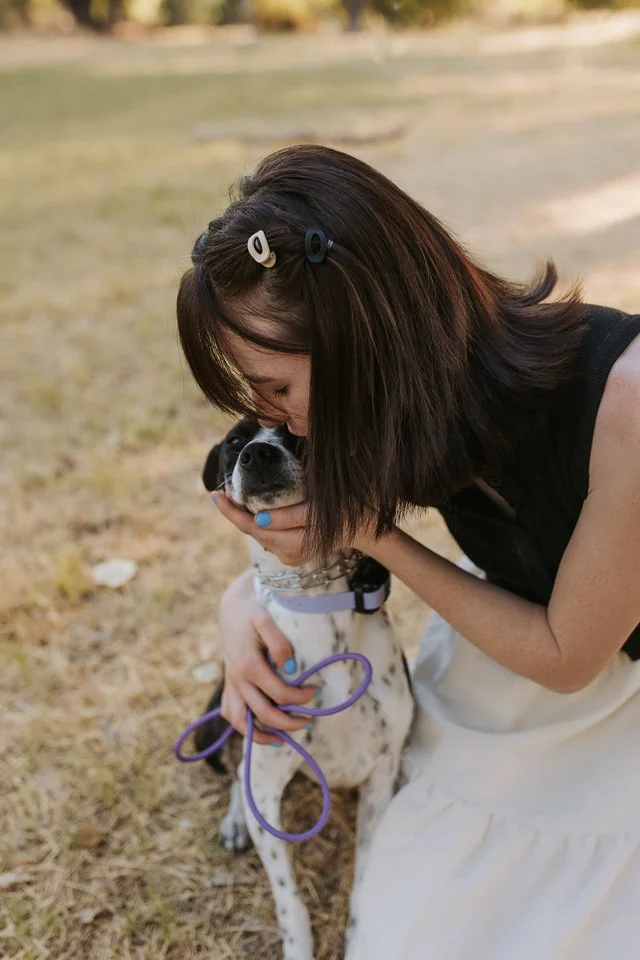 A woman affectionately hugging her dog outdoors in a grassy area.
