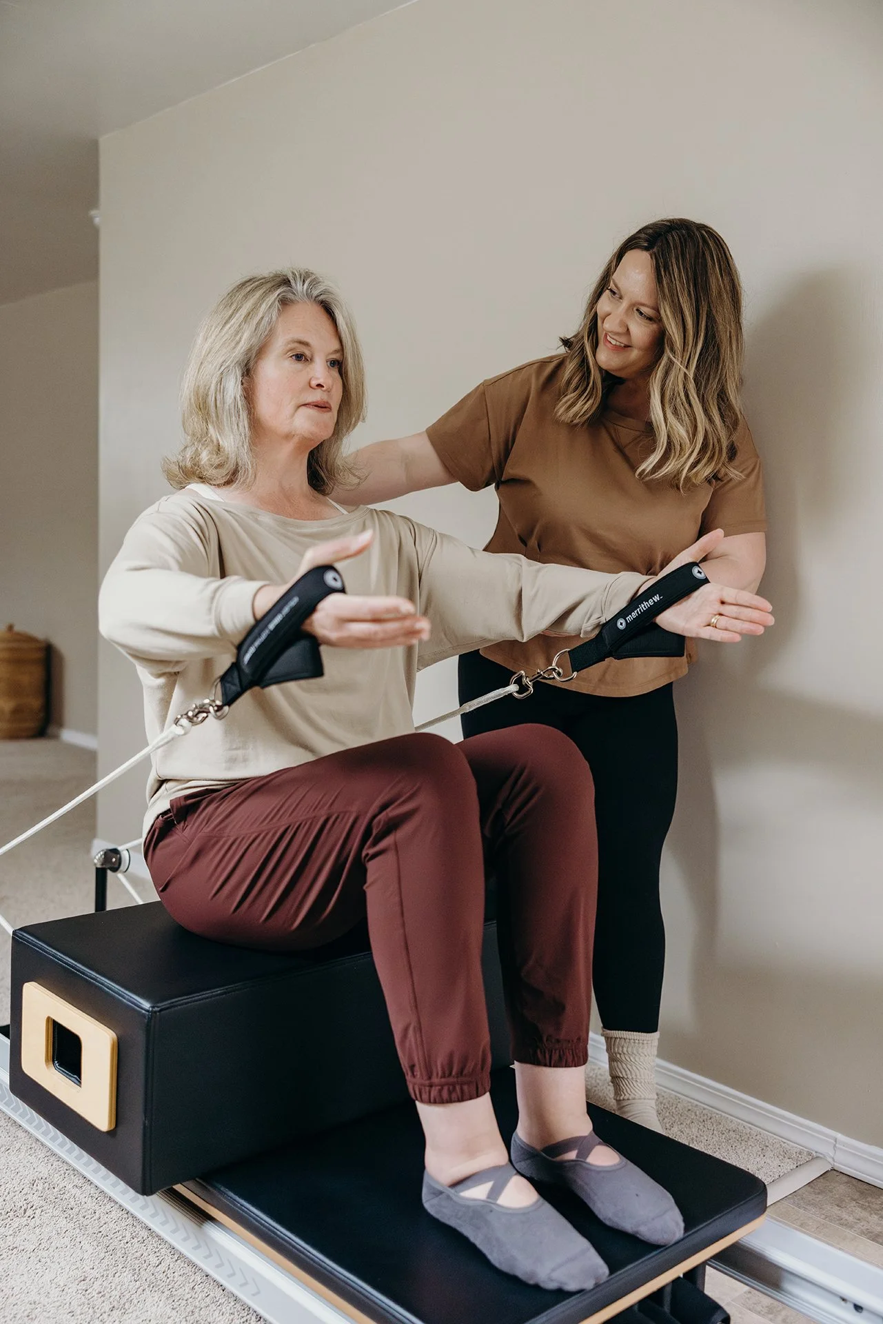 Pilates instructor, Jess, guiding a client through a seated arm-strengthening exercise on a reformer at Liro Pilates in Anchorage, Alaska