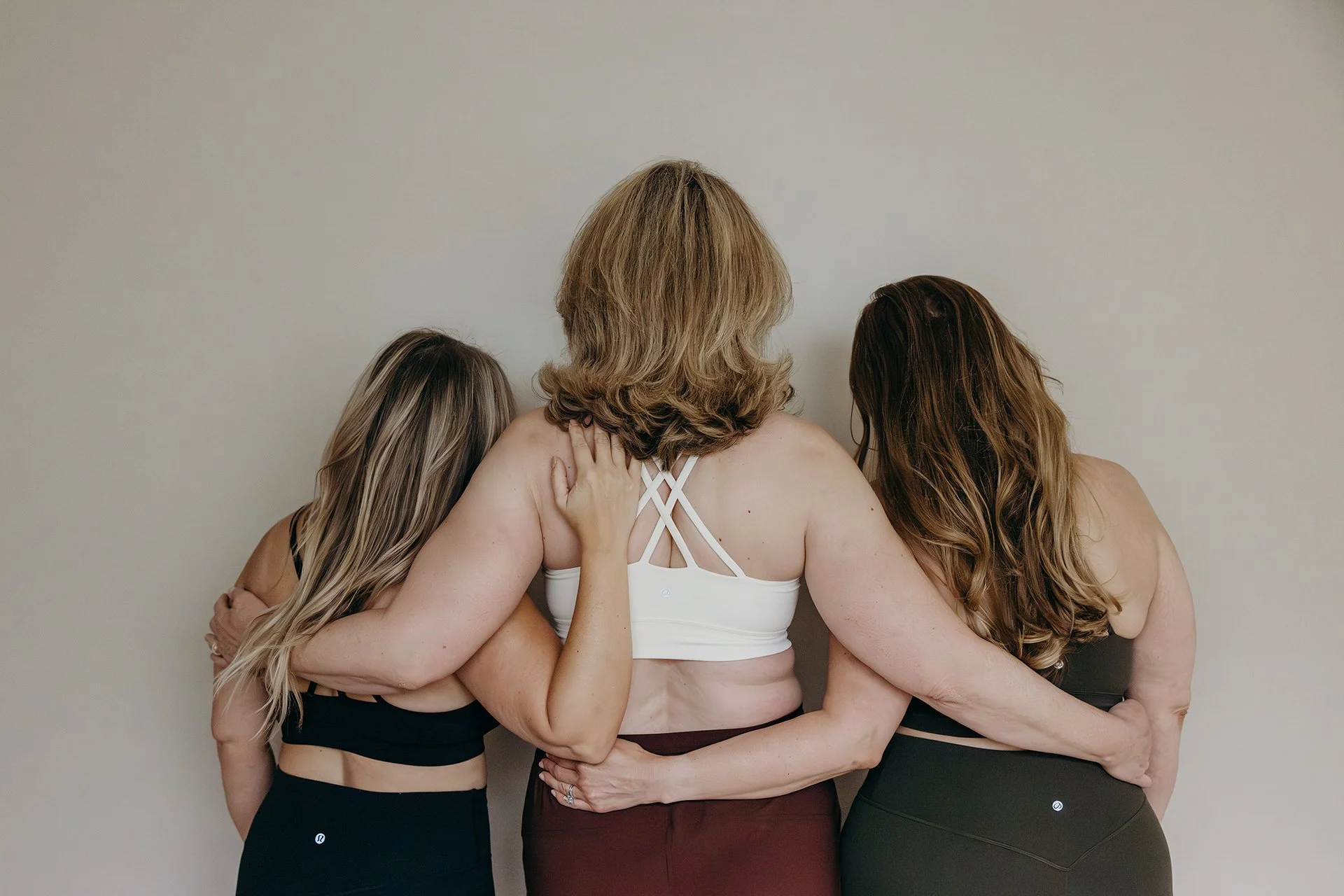 Three women in Pilates attire embracing at Liro Pilates in Anchorage, Alaska