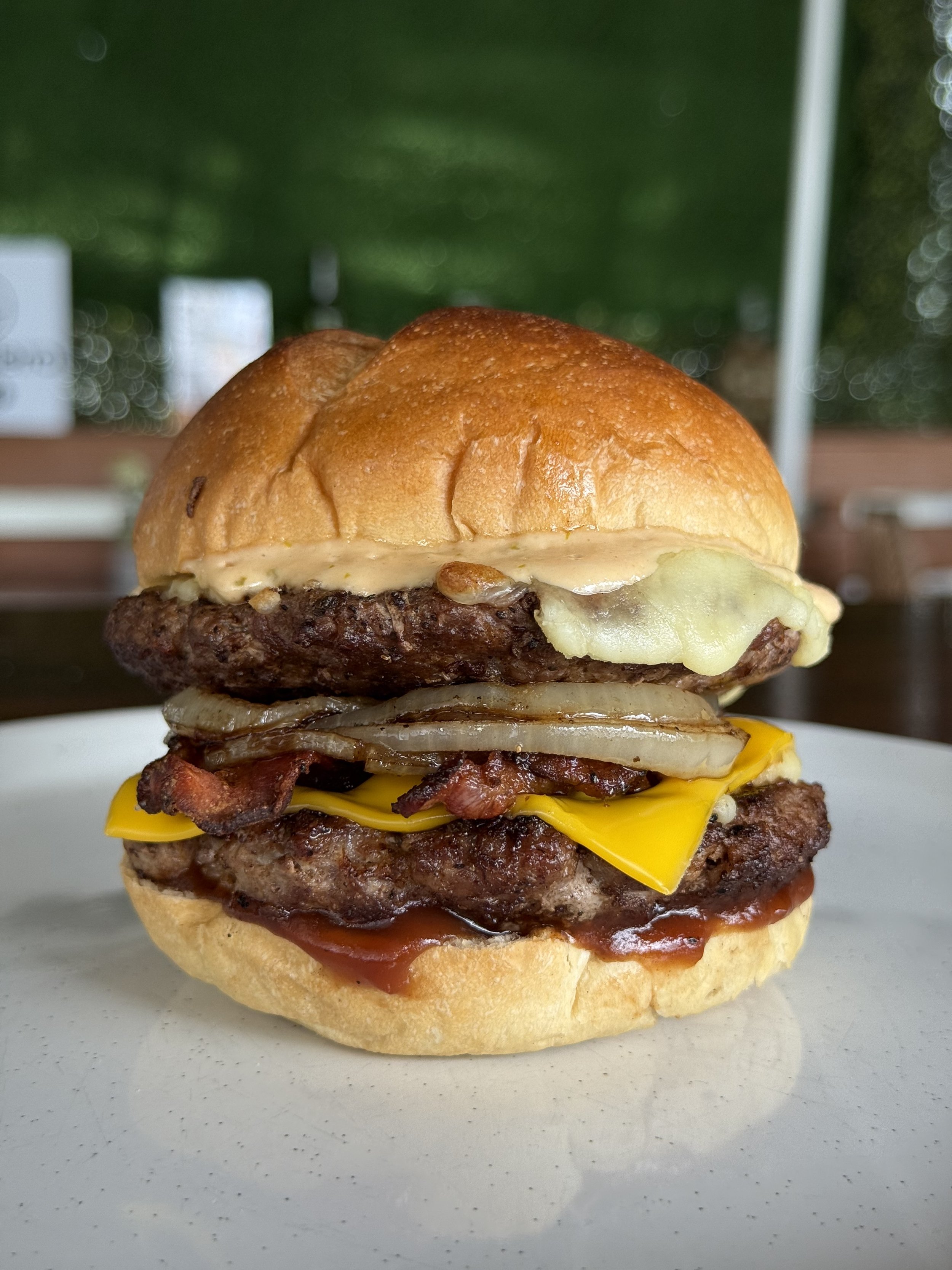 Hamburguesa con pan, carne, queso, tocino, cebolla, salsa y lechuga en plato blanco.