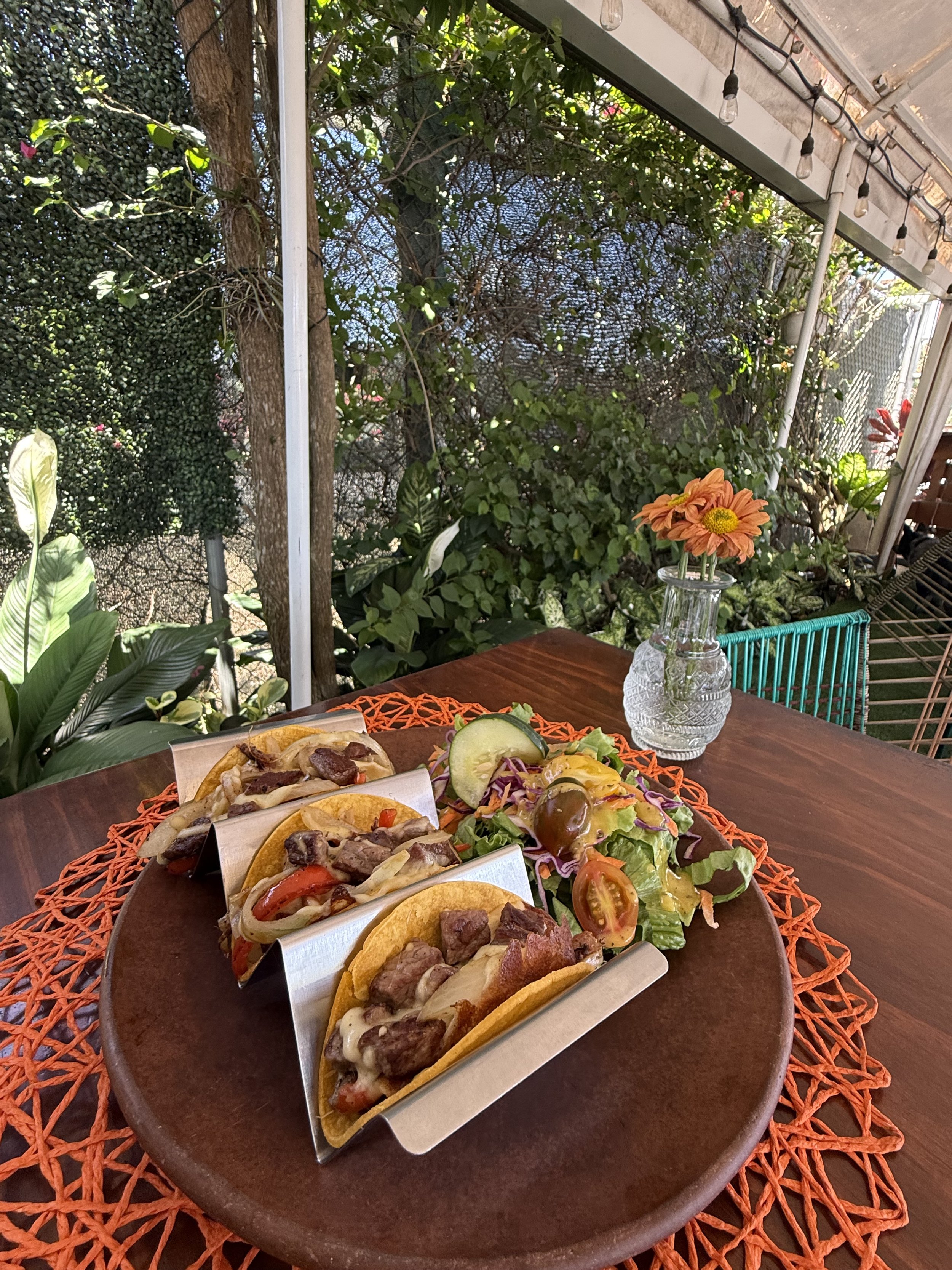 Un plato con tacos, ensalada y vegetales en un restaurante al aire libre con plantas y decoraciones de luz.