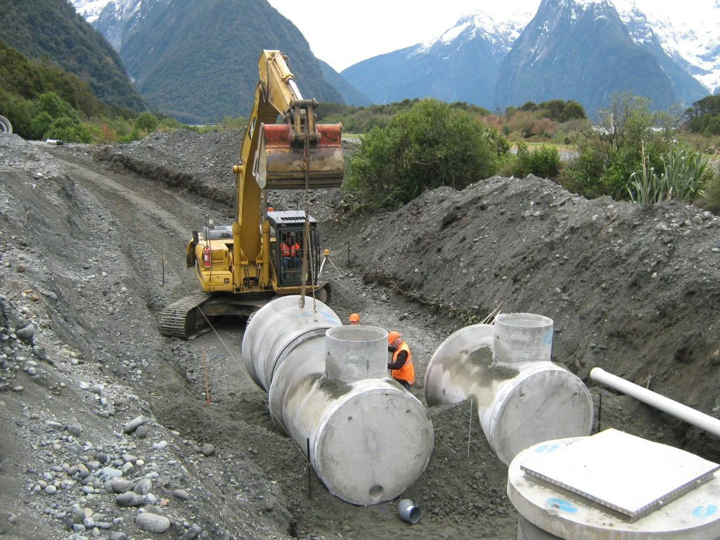 Construction workers installing large underground pipes with a bulldozer in a mountainous area.