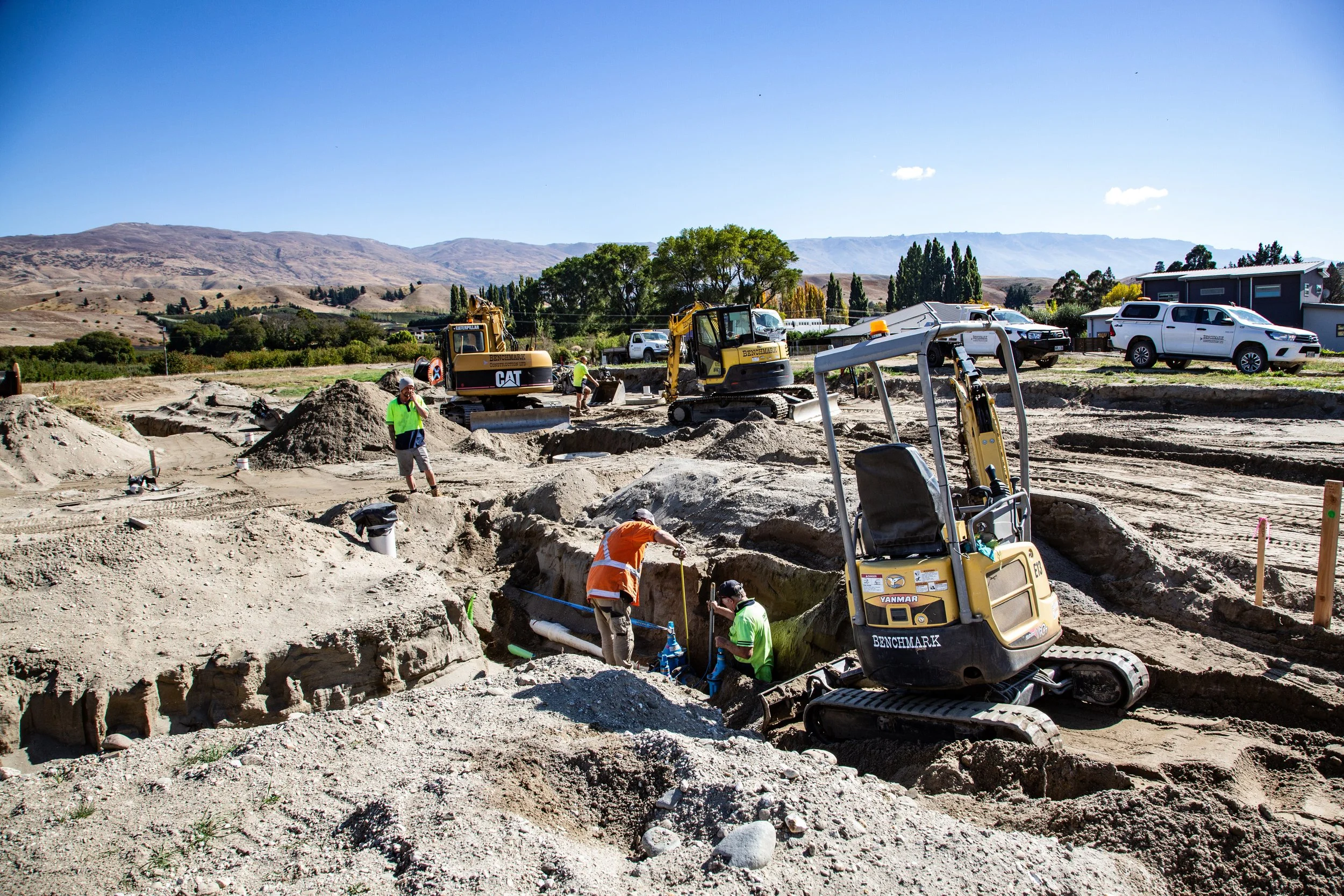 Earthworks and site preparation on construction workers building a foundation with excavators and digging trenches on a construction site in Central Otago with mountains in the background.