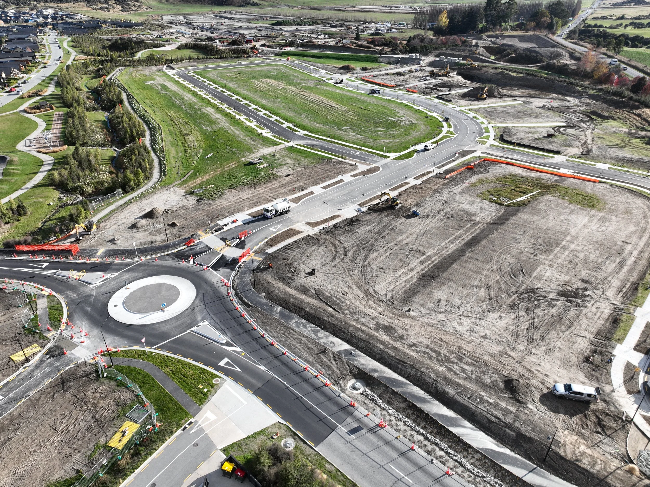 An aerial view of a residential subdivision development under construction with roads and pathways, trucks, and civil construction equipment, and areas of dirt and earthmoving in Queenstown.