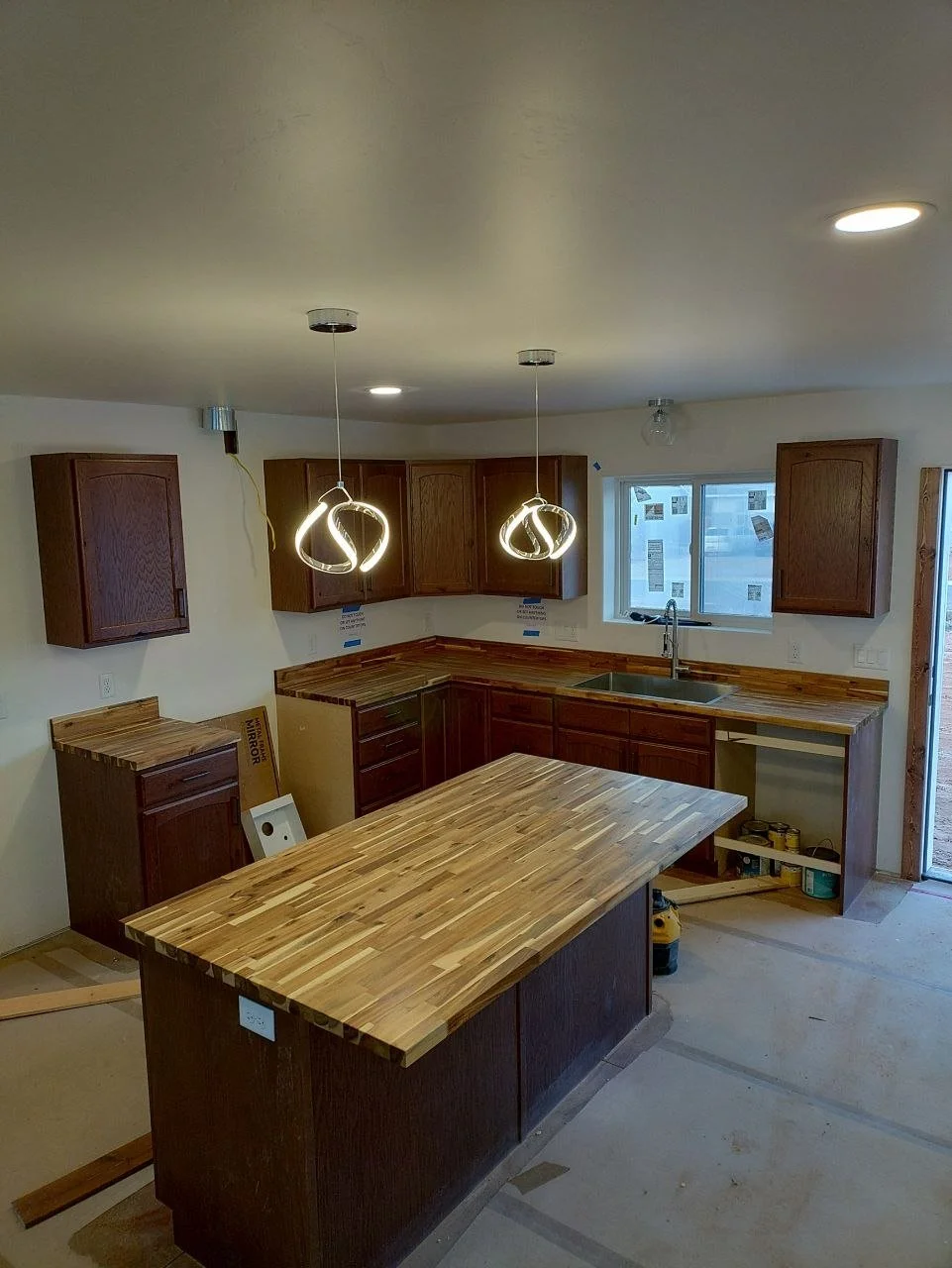 Kitchen under construction with wooden cabinets, a central island, and pendant lights hanging from the ceiling.